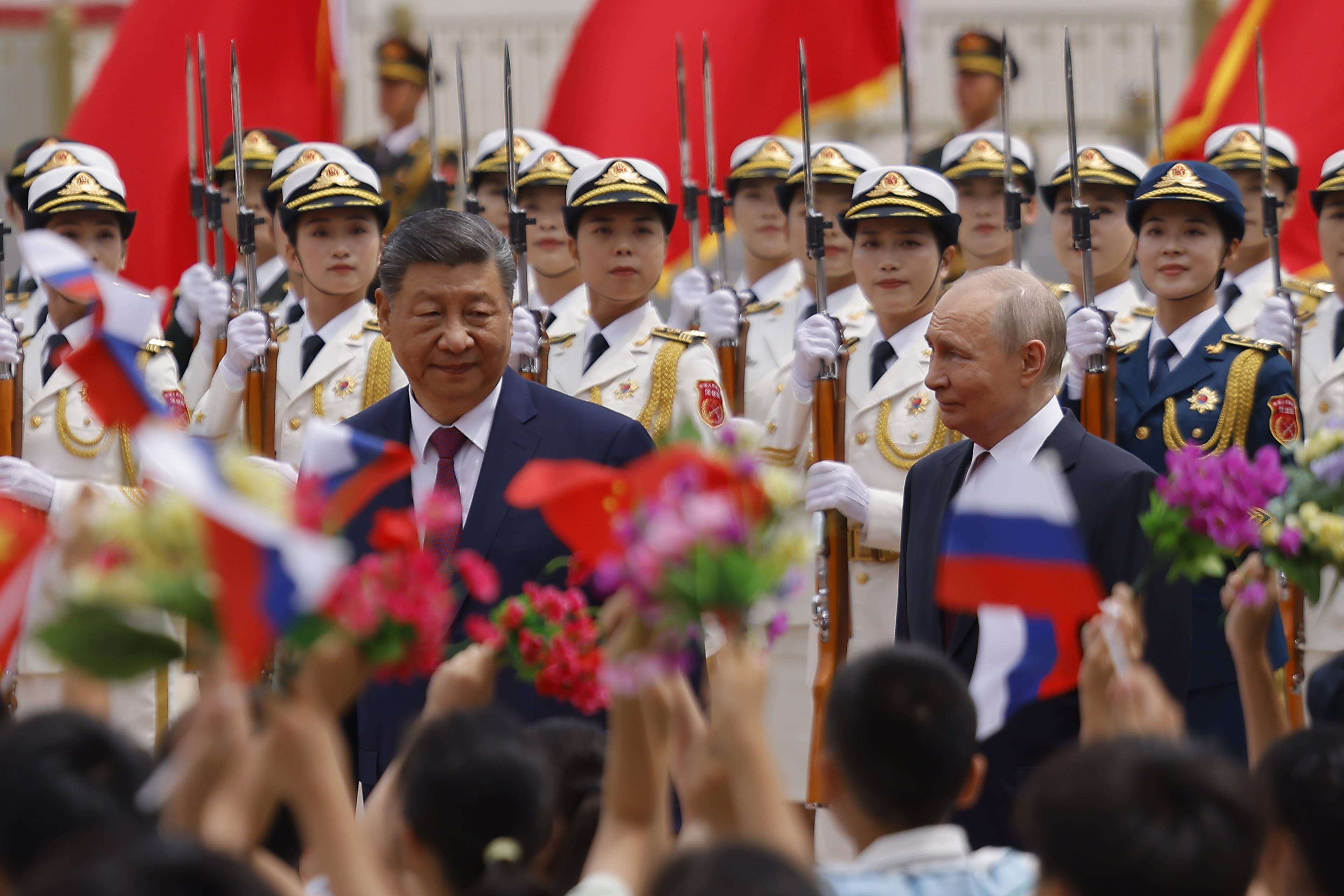 Kinas president Xi Jinping og Russlands president Vladimir Putin står side om side. Bak dem står en rekke soldater i hvite uniformer med rifler. I fremgrunnen holder barn oppe kinesiske og russiske flagg. (Bildebeskrivelsen er laget med hjelp av en KI-tjeneste)
