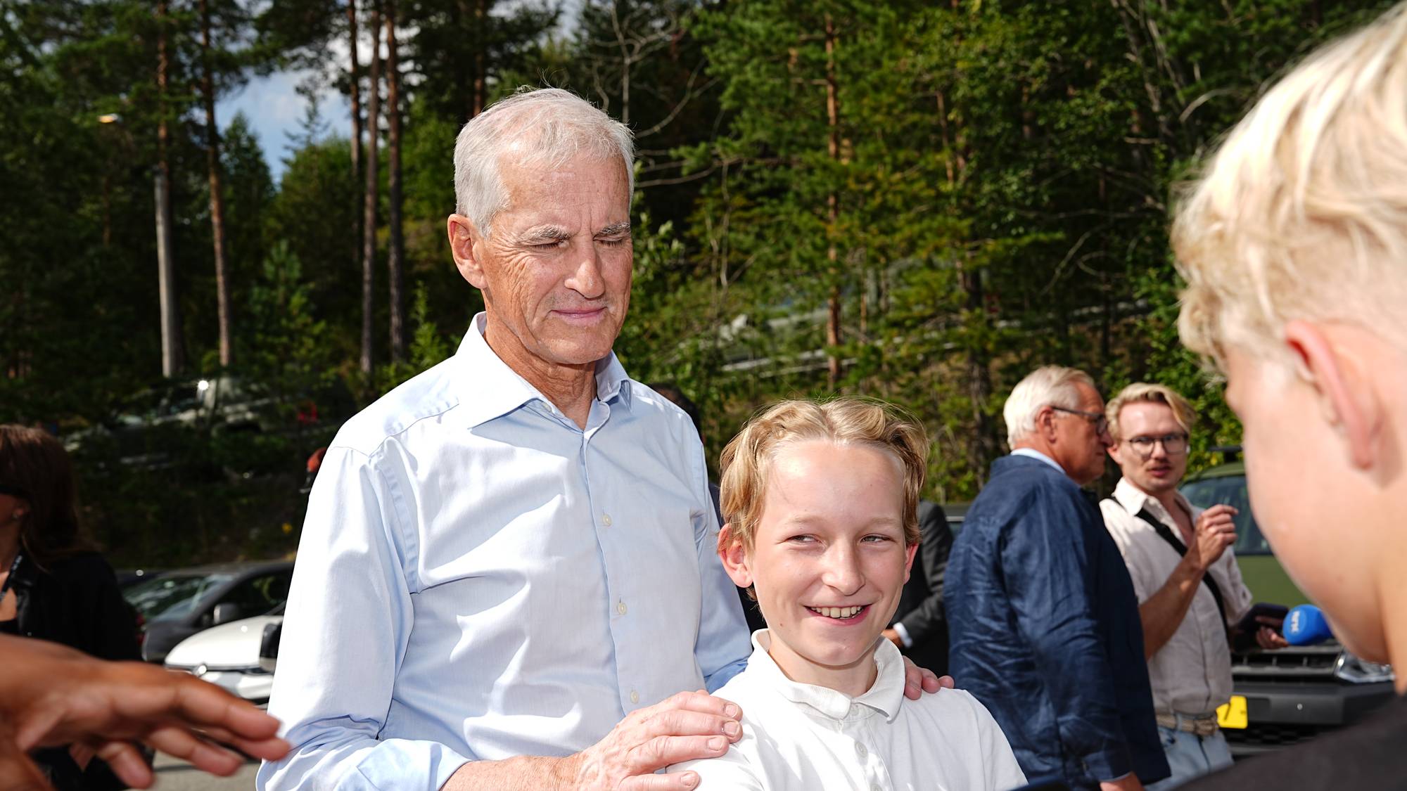 Statsminister Jonas Gahr Støre hilser på en gutt utendørs. Flere andre personer er i bakgrunnen. (Bildebeskrivelsen er laget av en KI-tjeneste)