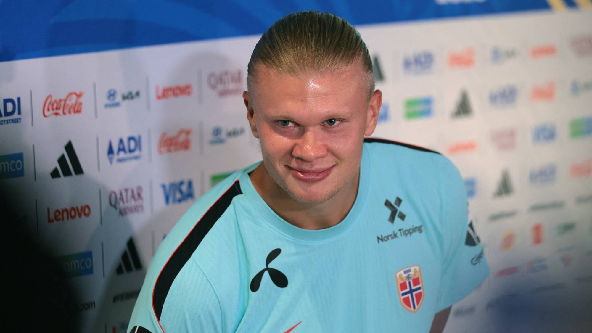 Erling Braut Haaland i lyseblå landslagsdrakt foran en sponsorfond. (Bildebeskrivelsen er laget av en KI-tjeneste)