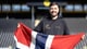 Niklas Aune Johnsen / Bodø/Glimt En mann med mørkt hår og skjegg som holder et norgeflagg på en fotballbane