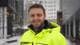 Nadir Alam / NRK En person iført en gul jakke med tekst fra Oslo kommune Bymiljøetaten står ute i snøvær. Bakgrunnen viser moderne bygninger med snødekte overflater. Det snør svakt, og omgivelsene virker stille. Personen ser inn i kameraet, og det er lite aktivitet rundt.