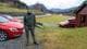 Håkon Vatnar Olsen / NRK En person står foran tre biler på en grusvei med fjell og bakker i bakgrunnen. Det er en rød bil til venstre, og en annen rød bil til høyre ved en bygning. Omgivelsene viser et grønt landskap under en overskyet himmel. Veien i bakgrunnen er delvis synlig.