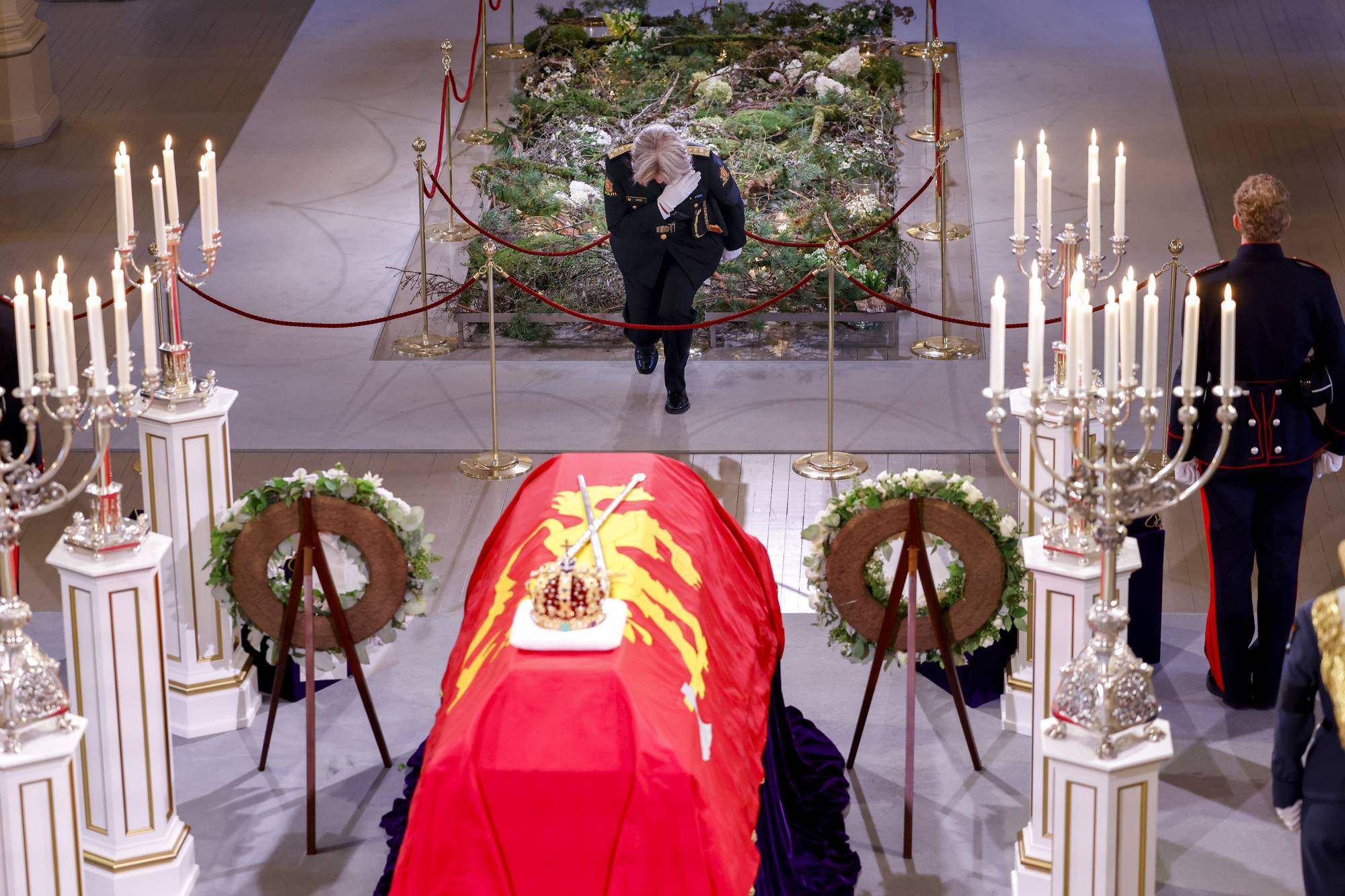 En kvinne i uniform bukker foran en båre dekket av et flagg i en kirke. (Bildebeskrivelsen er laget av en KI-tjeneste)