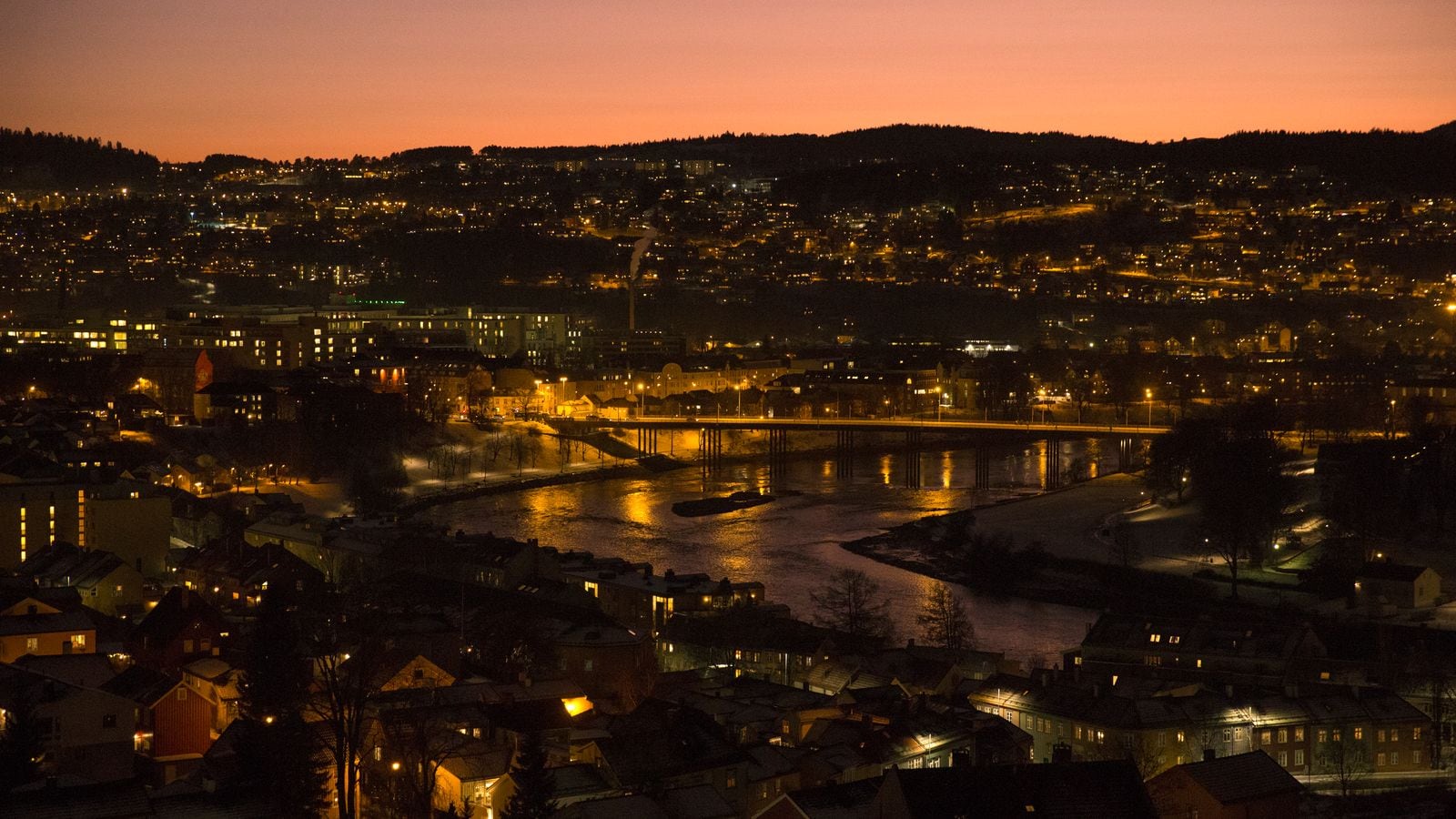 Trondheim by på kvelden med rødskjær på himmelen og lysene som glitrer.