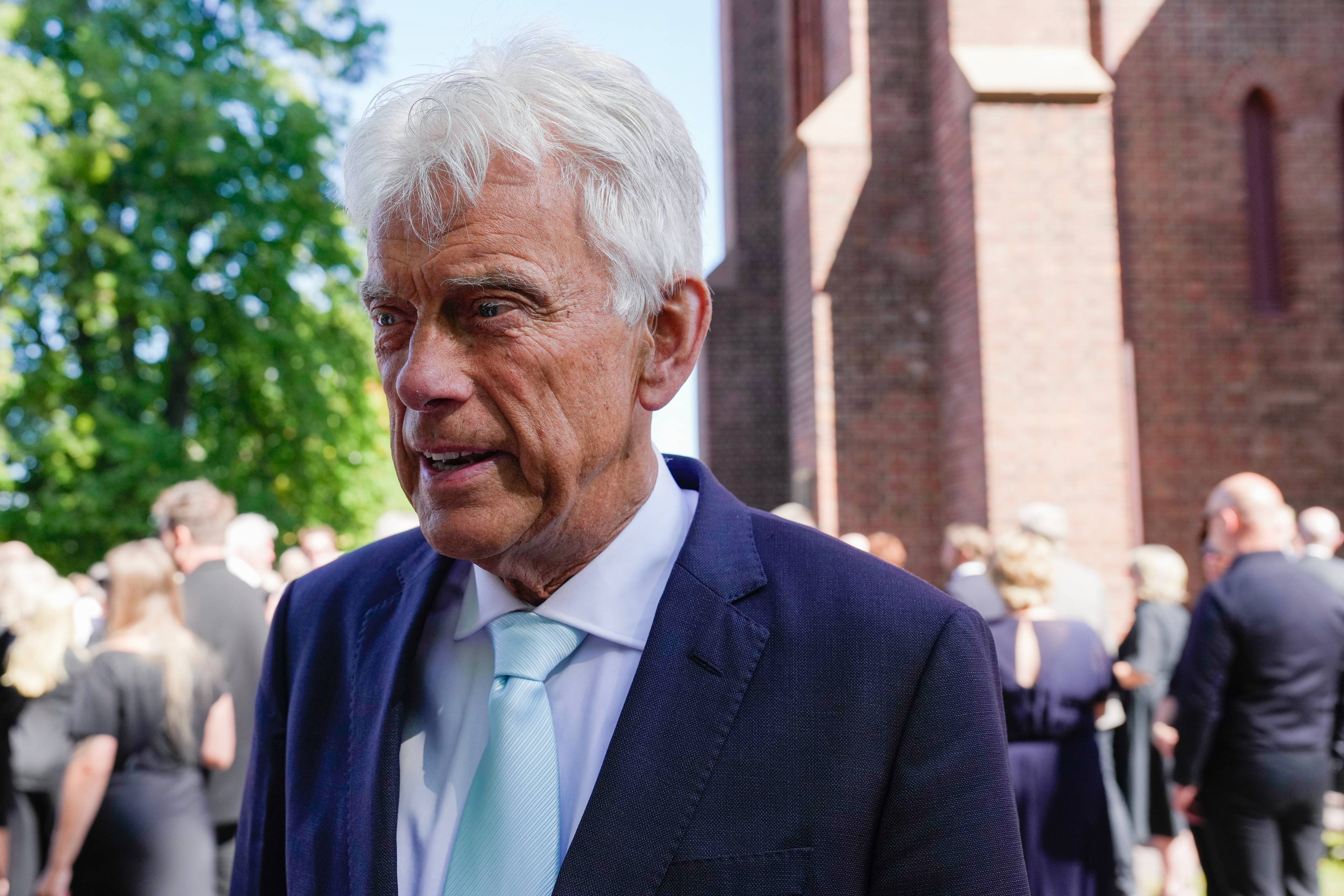 Bjørge Stensbøl står utendørs ved en kirke med folk i bakgrunnen.