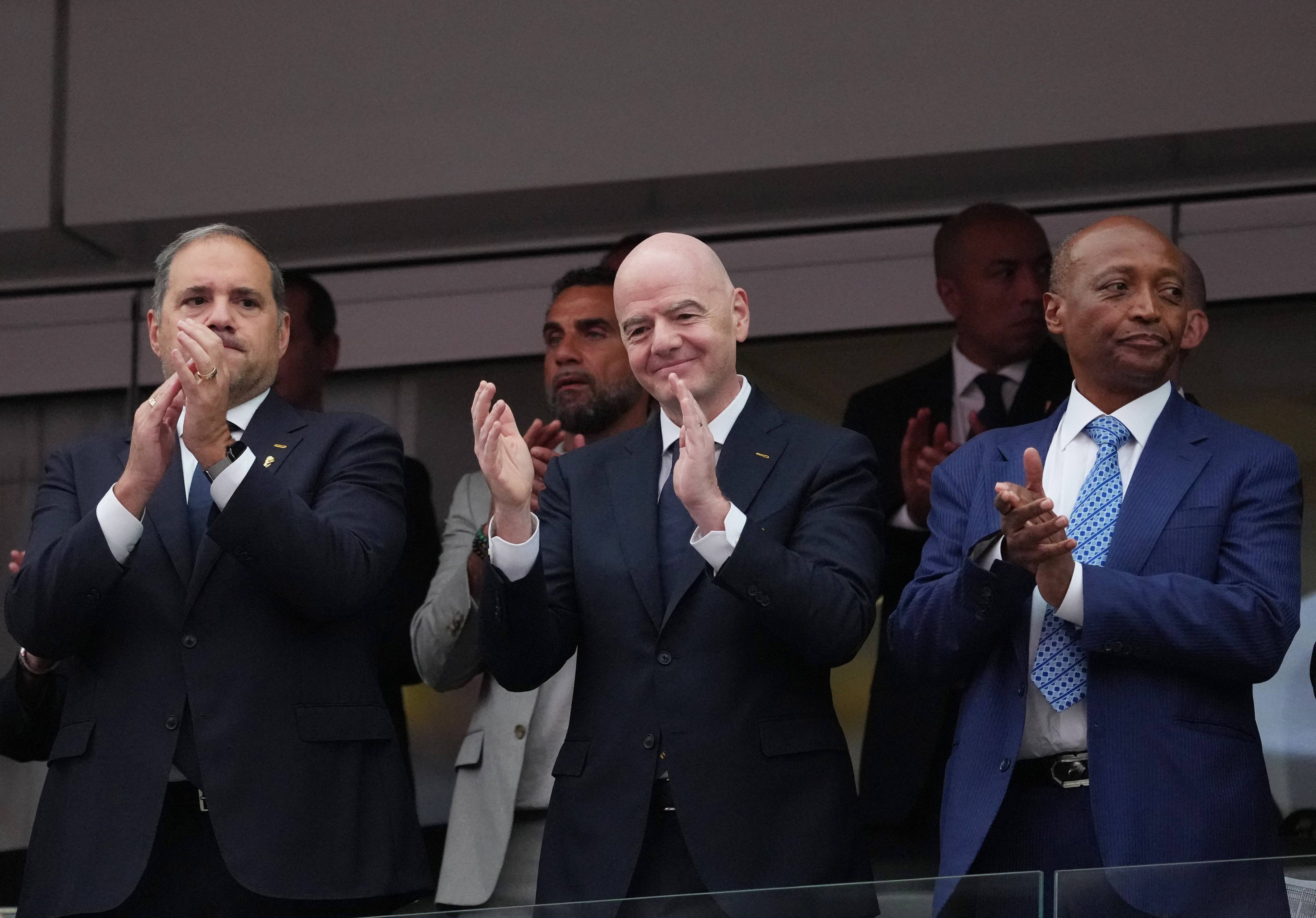 FIFA-president Gianni Infantino og andre menn i dress klappar på tribunen under ein fotballkamp. (Bildebeskrivelsen er laget av ein KI-teneste)