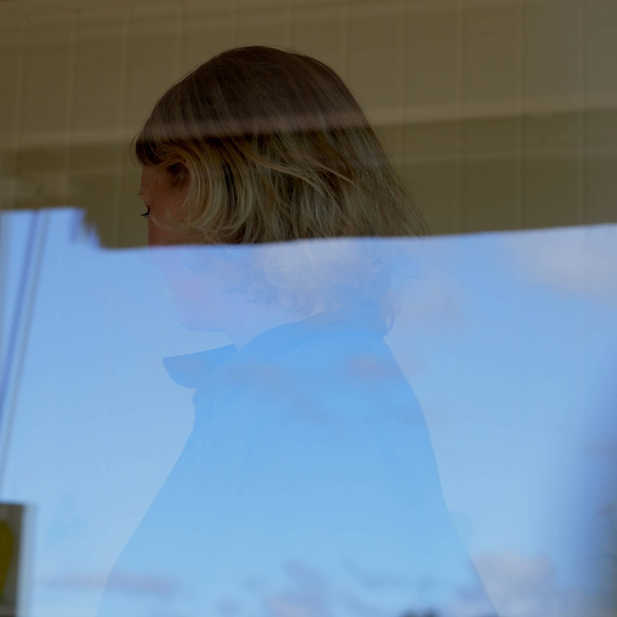bakhodet til en kvinne som ser ned, speilrefleks i vinduet skjuler ansiktet og store deler av kroppen