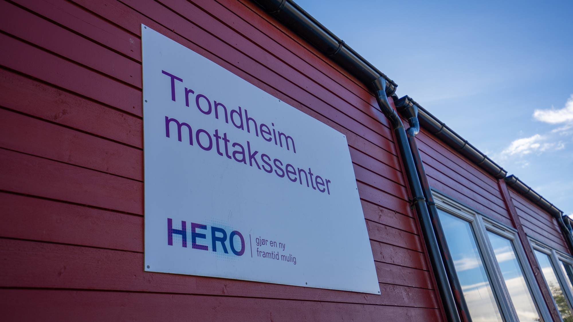 Skilt på rød trevegg ved Trondheim mottakssenter driftet av Hero. (Bildebeskrivelsen er laget av en KI-tjeneste)