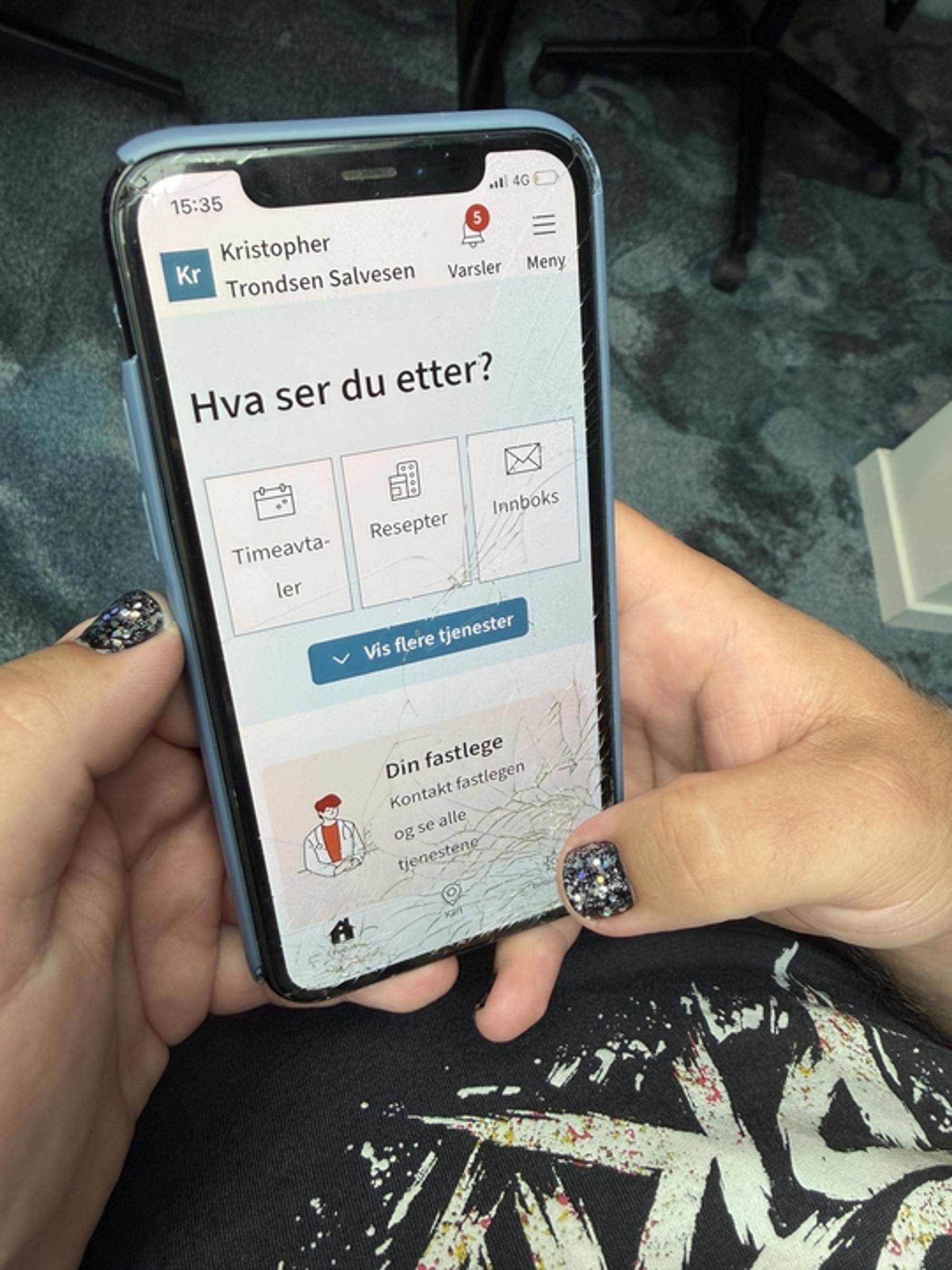 En person holder en iPhone med knust skjerm. På skjermen er han logget inn på Helsenorge sine sider