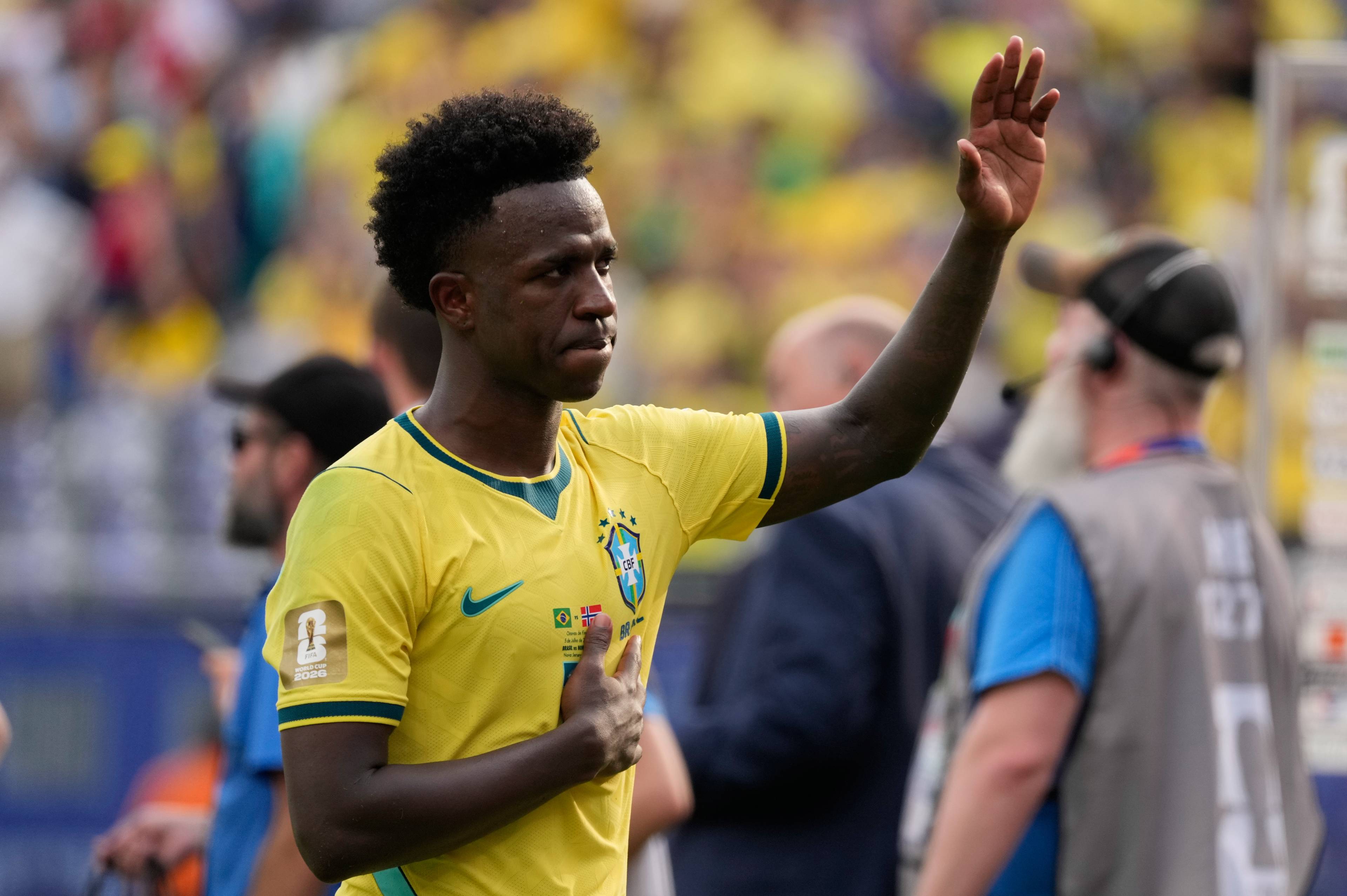 Fotballspilleren Vincius Jnior i gul landslagsdrakt vinker til publikum på stadion. (Bildebeskrivelsen er laget av en KI-tjeneste)