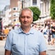 Per-Kåre Sandbakk / NRK En mann med kort, grått hår og blå skjorte står i en gate. I bakgrunnen ser man mange folk.