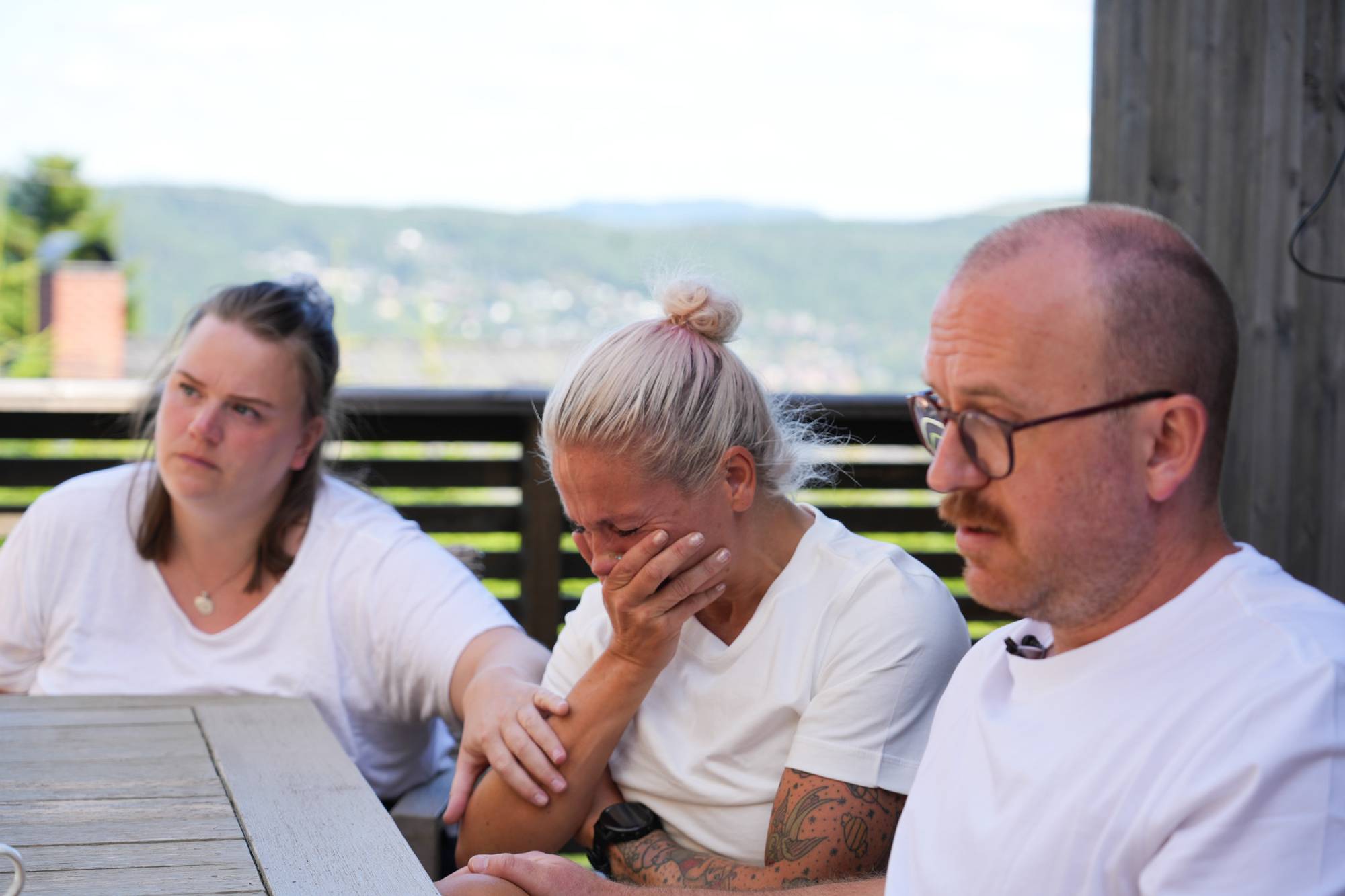 Tre personer som sitter ute. En gråter og en annen trøster. 