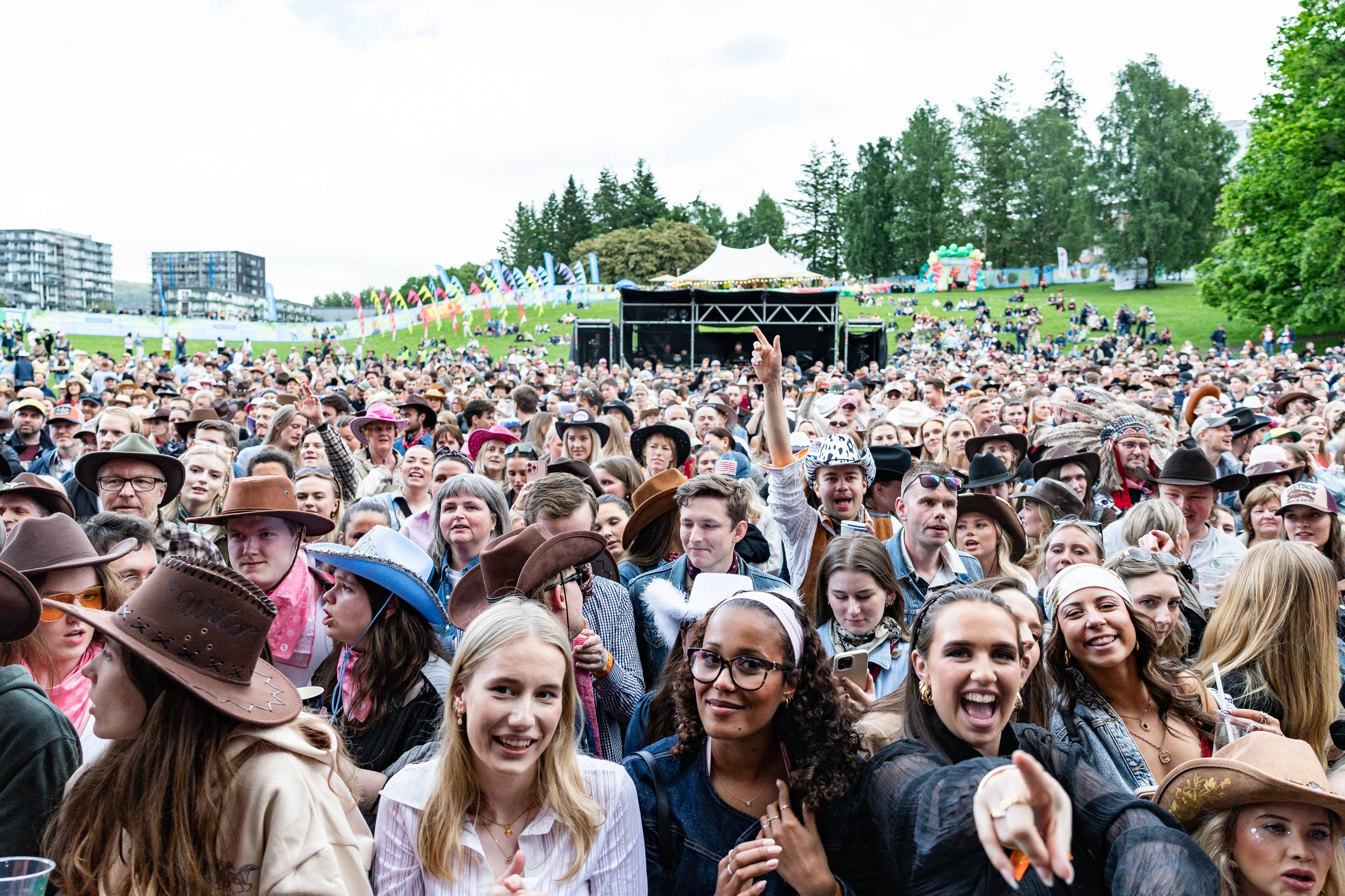 Publikum på en utendørsfestival. Mange har på seg cowboyhatter. En scene med lys og lydutstyr er synlig i bakgrunnen. (Bildebeskrivelsen er laget av en KI-tjeneste)