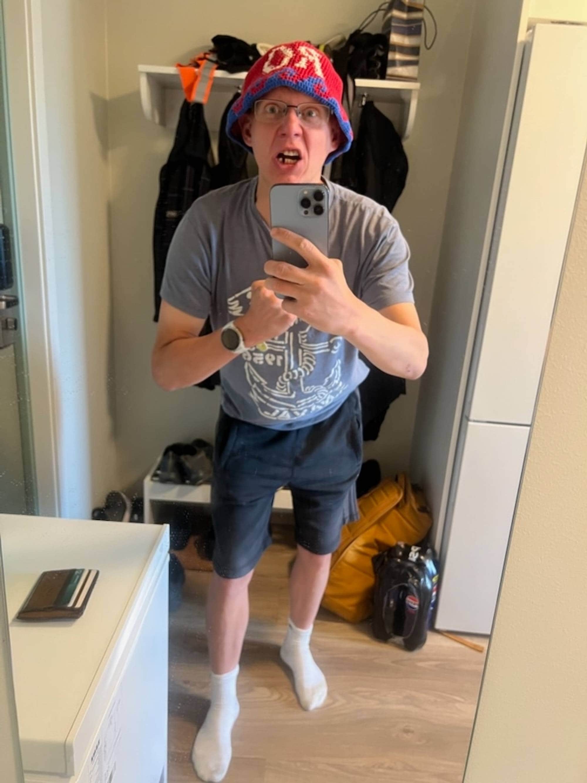 En mann tar bilde av seg selv i speilet. Han har på en heklet bøttehatt i rødt og blått. 