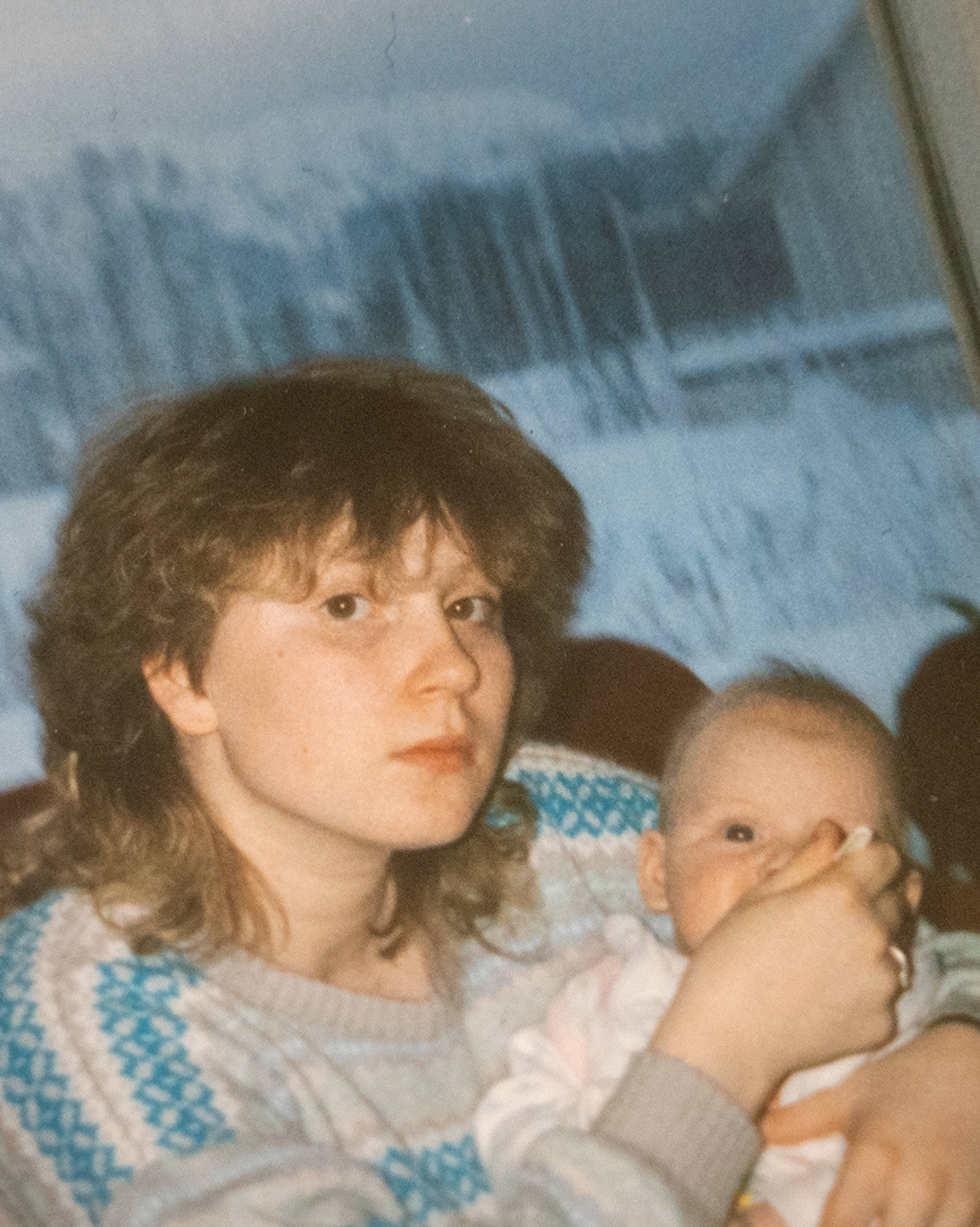 Ung mor  med halvlangt hår og mønstret genser mater babyen sin, vindu i bakgrunnen