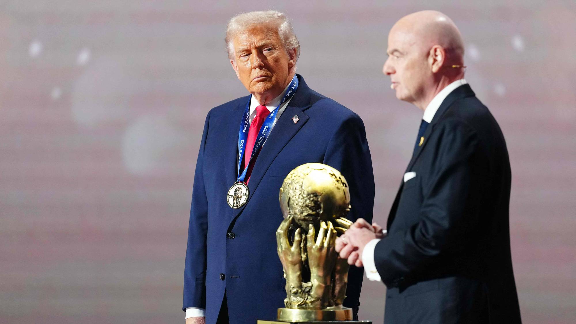 Donald Trump og Gianni Infantino står ved siden av en premie. Trump har en medalje rundt halsen. Prisen er en gullklode støttet av hender. (Bildebeskrivelsen er laget av en KI-tjeneste)