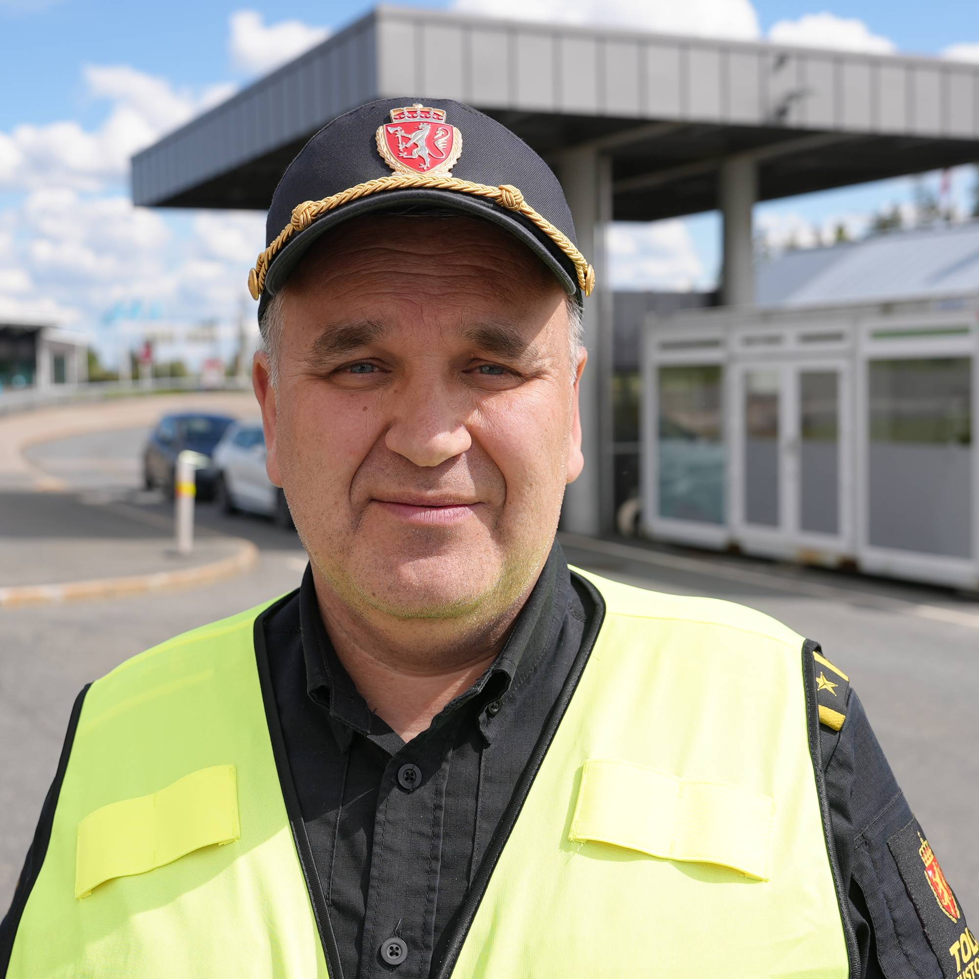 Et portrett av en mann i svart uniform med gul vest. Han jobber for tolletaten. 