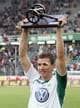 RONNY HARTMANN / DDP,NTB En fotballspiller holder en pokal med en kanon i tre. Han er iført en hvit trøye med grønn krage og V-formet logo. Bak ham er et publikum på en stadion. (Bildebeskrivelsen er laget av en KI-tjeneste)