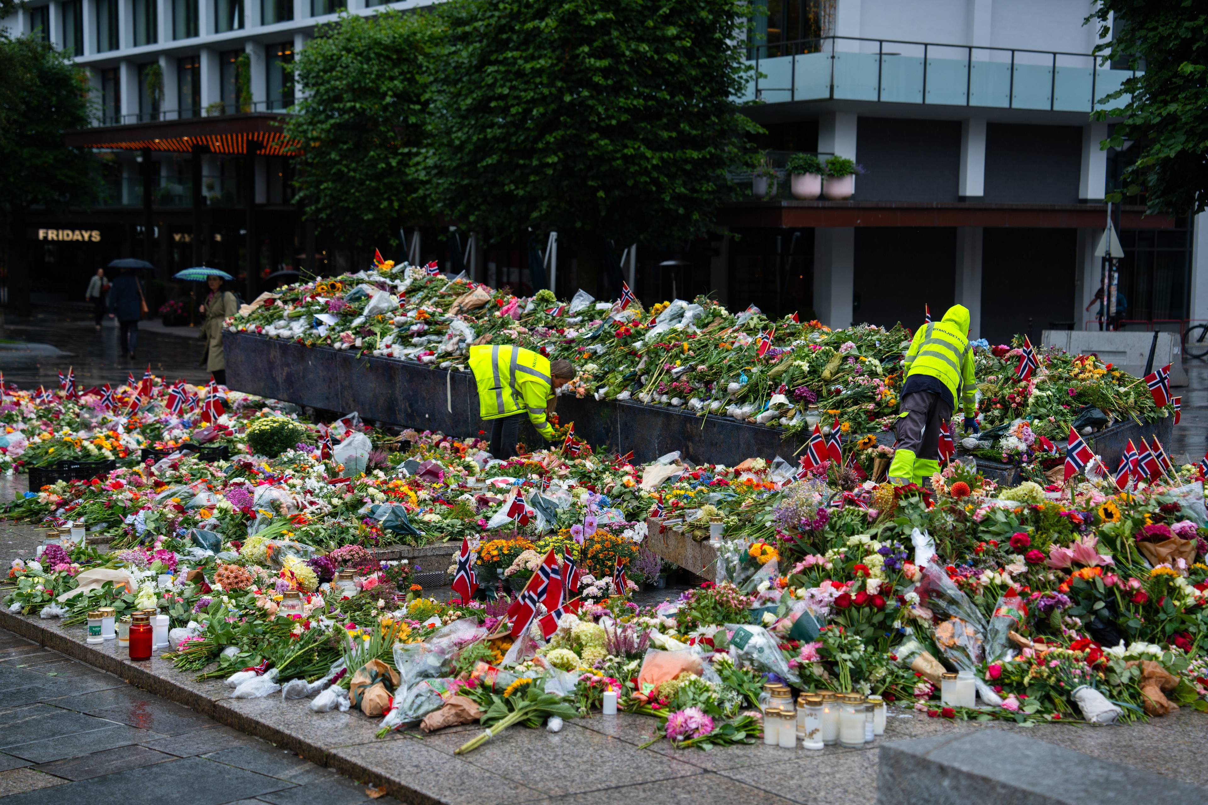 Den blå steinen i Bergen er dekket av blomar, flagg og kort for å heidre den avdøde kong Harald. To menneske i gule arbeidsklede står midt i blomsterhavet og ryddar bort visne blomster.