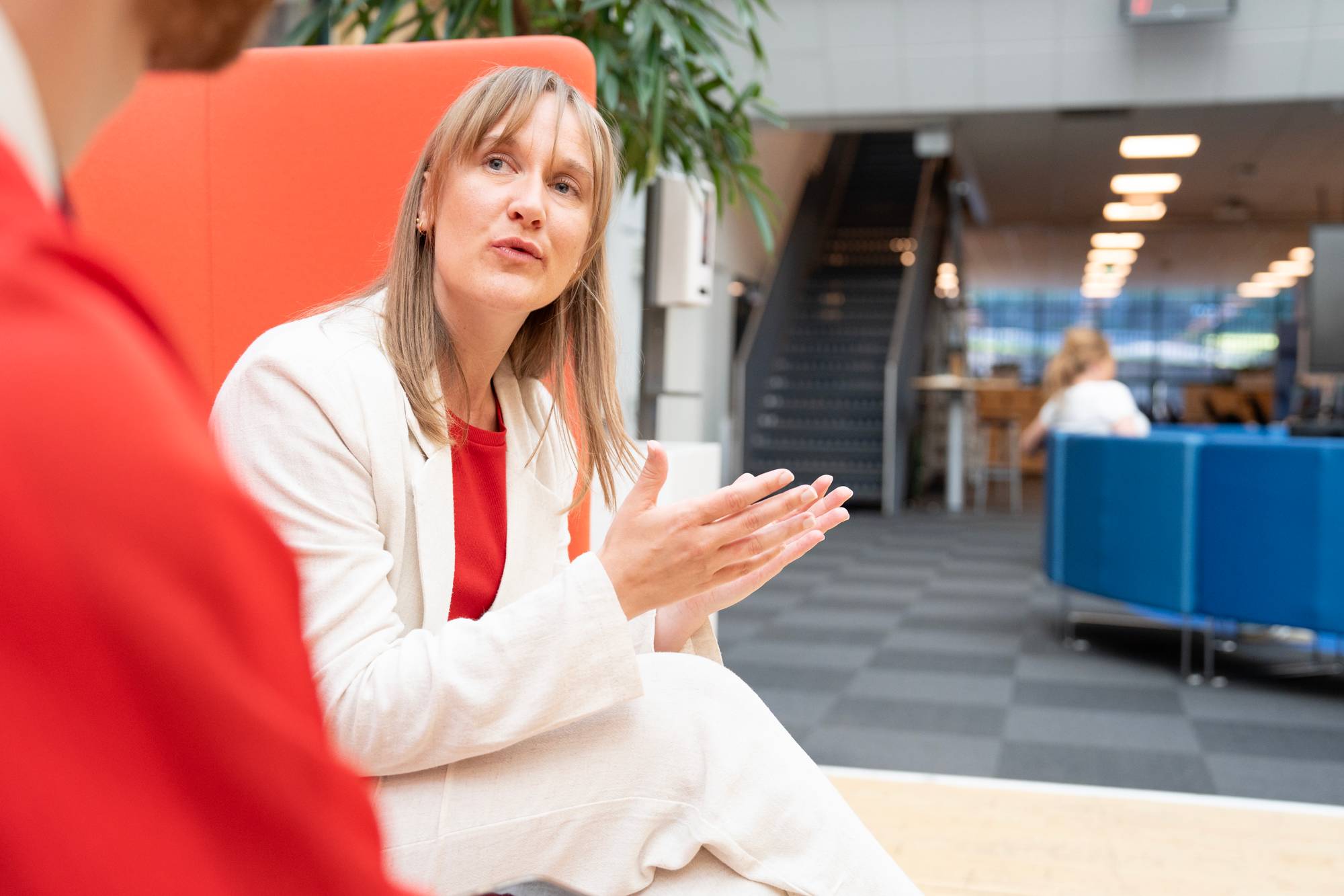Kvinne i hvit dress snakker med en person i et kontorlandskap. (Bildebeskrivelsen er laget av en KI-tjeneste)