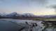 Foto: Tore Meek / NTB Bilde av et spektakulært landskap med snødekte fjell og isdekte detaljer ved en strandlinje. Vannet reflekterer den grå himmelen, mens en vei snor seg gjennom dalen. Omgivelsene gir inntrykk av arktisk klima, typisk for områder nær polarregionen. Bildet viser en fossefallslignende formasjon der is og sand møtes.