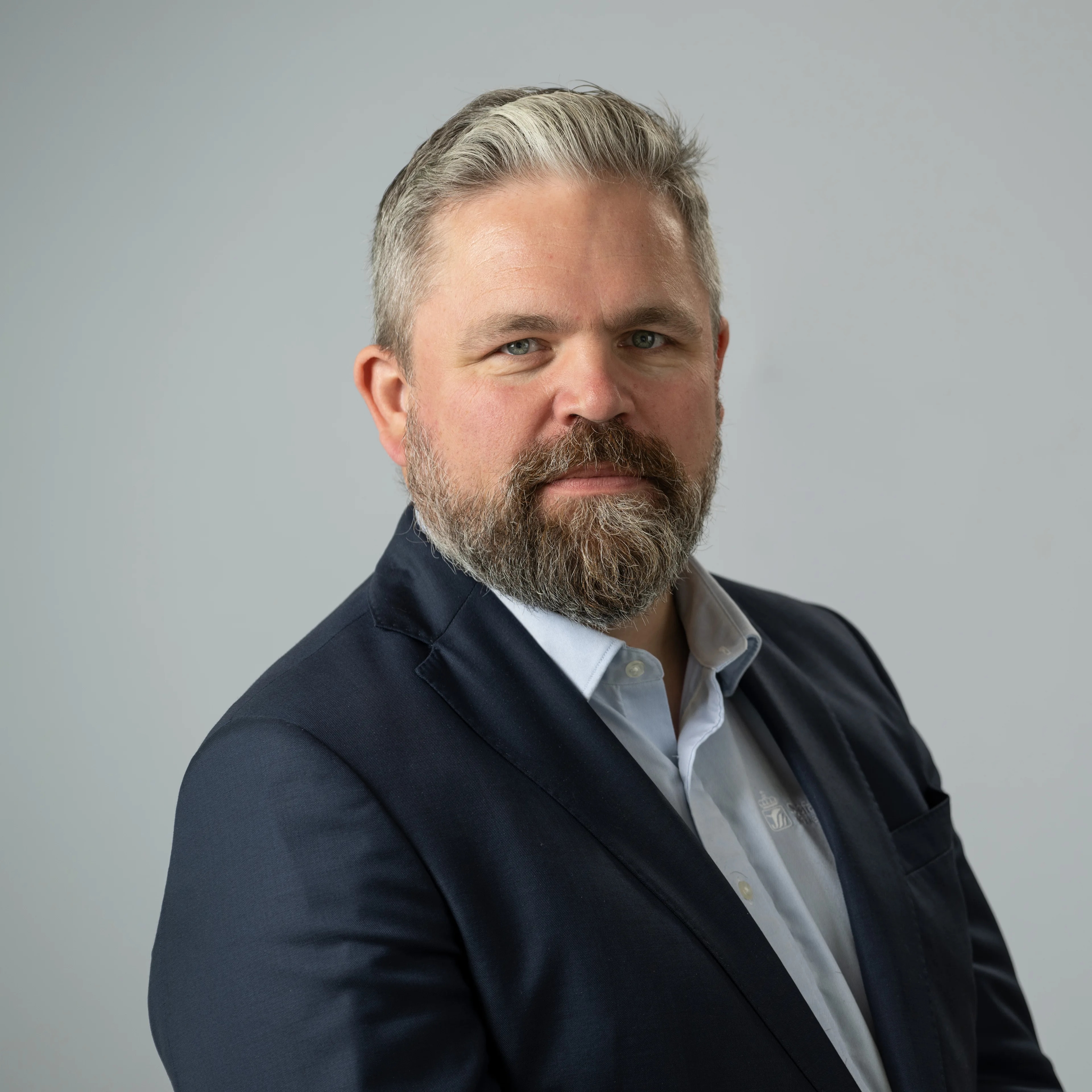 Bilde tatt i fotostudio av  Håvard Gåseidnes, avdelingsdirektør for fartøy og sjøfolk i Sjøfartsdirektoratet. Han har kort grålig hår, skjegg, mørk dress og blå skjorte. Står i profil og ser i kamera.