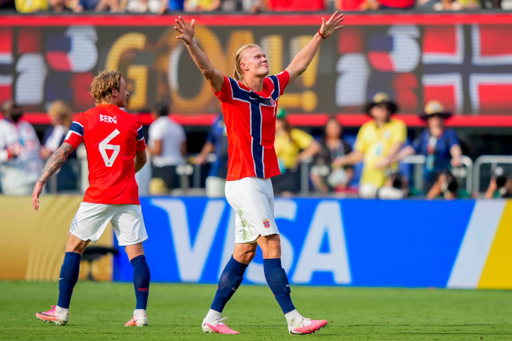 Erling Braut Haaland jubler i norsk landslagsdrakt med armene hevet på en fotballbane. (Bildebeskrivelsen er laget av en KI-tjeneste)