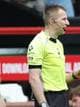 DARREN STAPLES / AFP,NTB Dommer i gult og svart. Han er på en fotballbane, med røde seter og mursteinsvegger bak seg. Dommeren har en mikrofon ved øret. Bak ham er det andre personer. (Bildebeskrivelsen er laget av en KI-tjeneste)