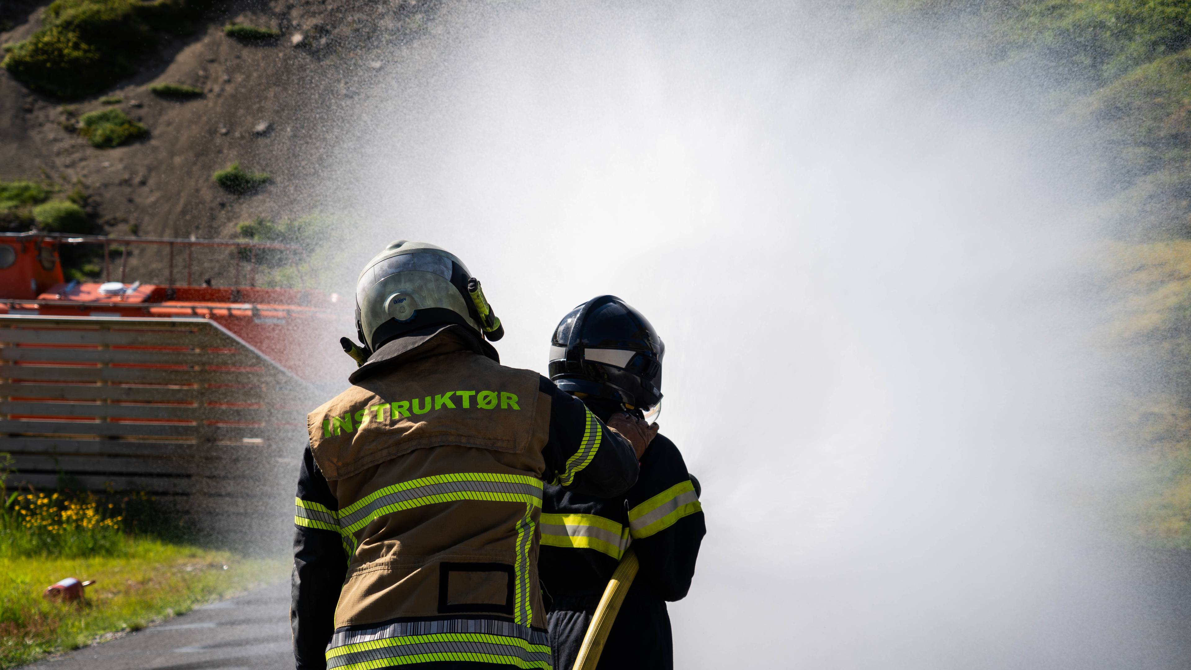 Branninstruktør veileder person i bruk av brannslange med vannsprut.