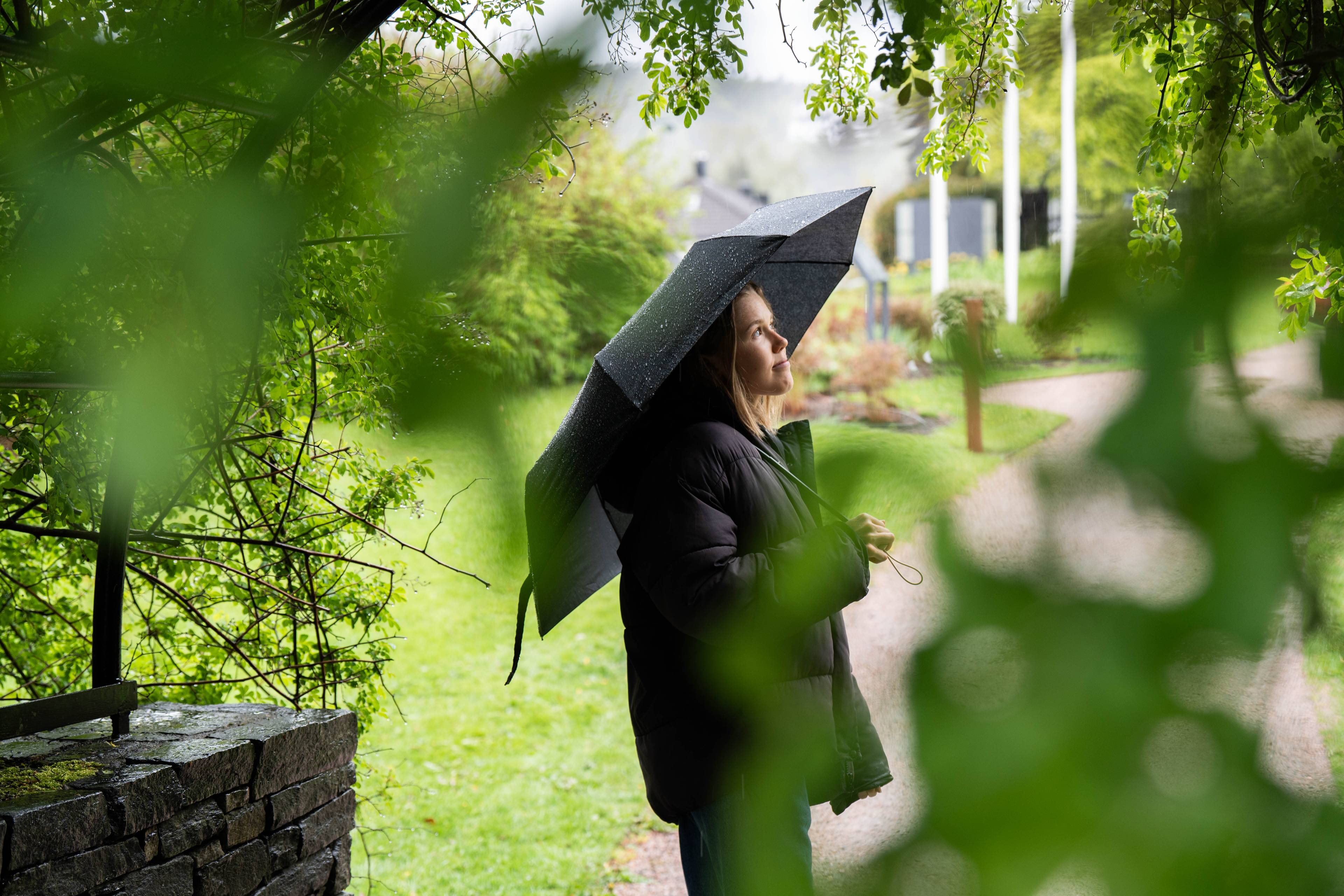 Hannah står under en paraply i en frodig hage.