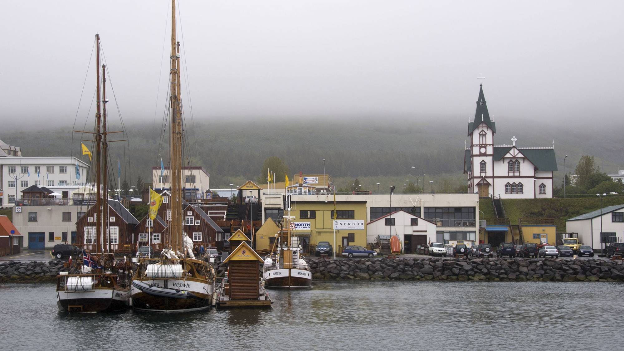 Seilskip ligger til kai i havnen i Húsavík på Island, med en kirke i bakgrunnen. (Bildebeskrivelsen er laget av en KI-tjeneste)