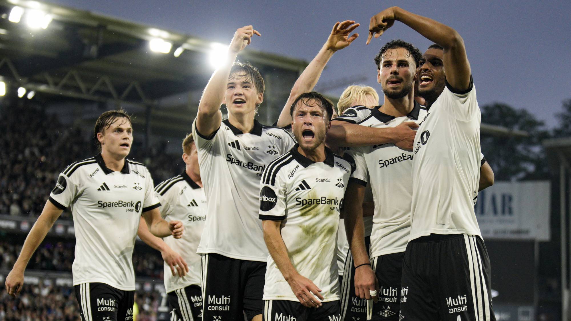 Rosenborg-spillere jubler sammen på banen etter scoring i en fotballkamp. (Bildebeskrivelsen er laget av en KI-tjeneste)