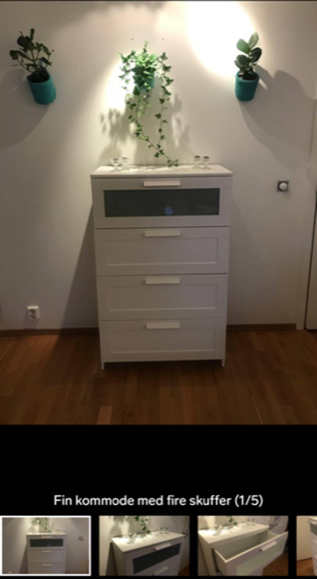 Hvit kommode inntil hvit vegg med grønne planter hengende over.