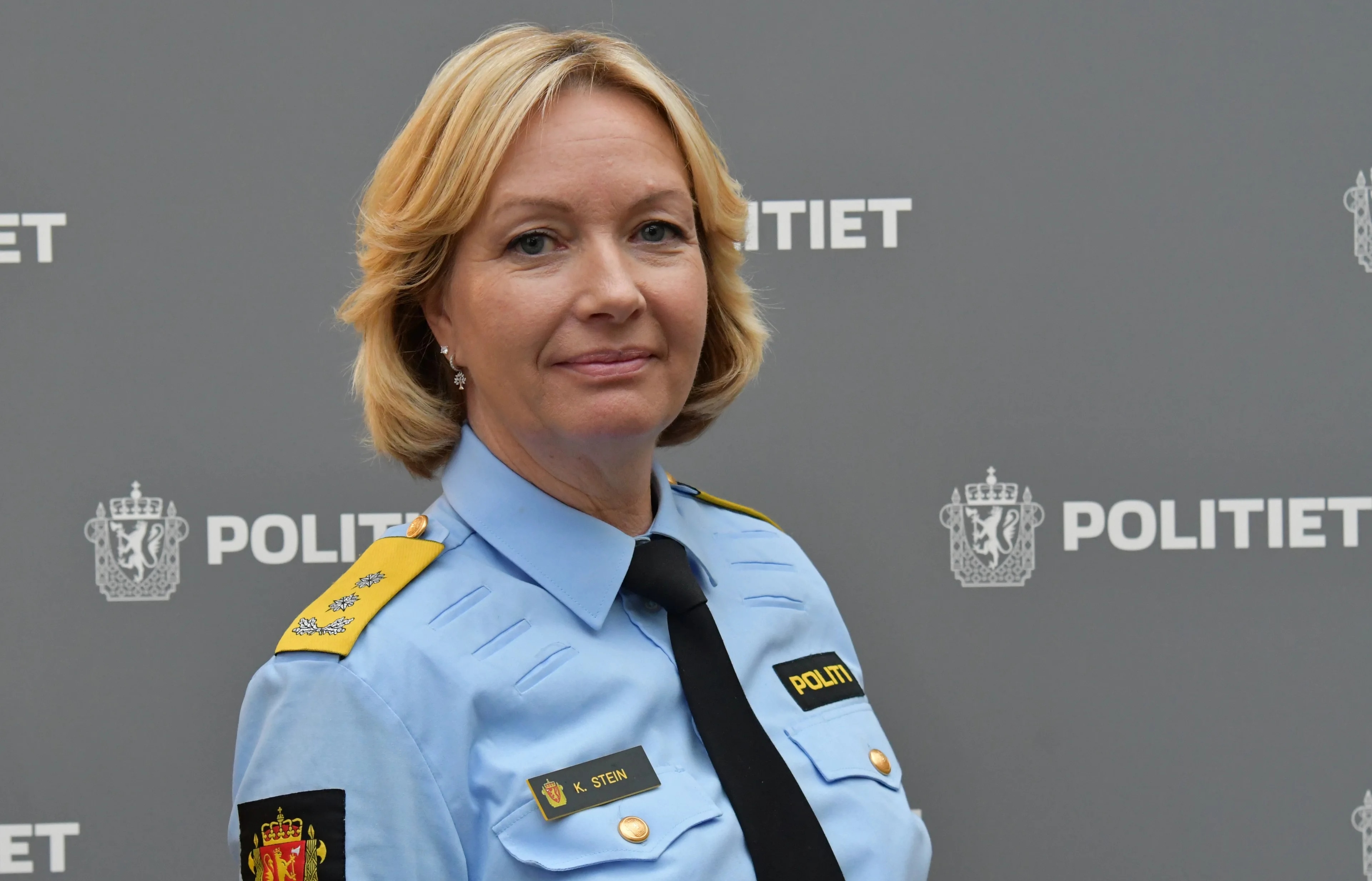 Bilde viser overkroppen av en blond kvinne med halvlangt hår i blå politiskjorte og slips.