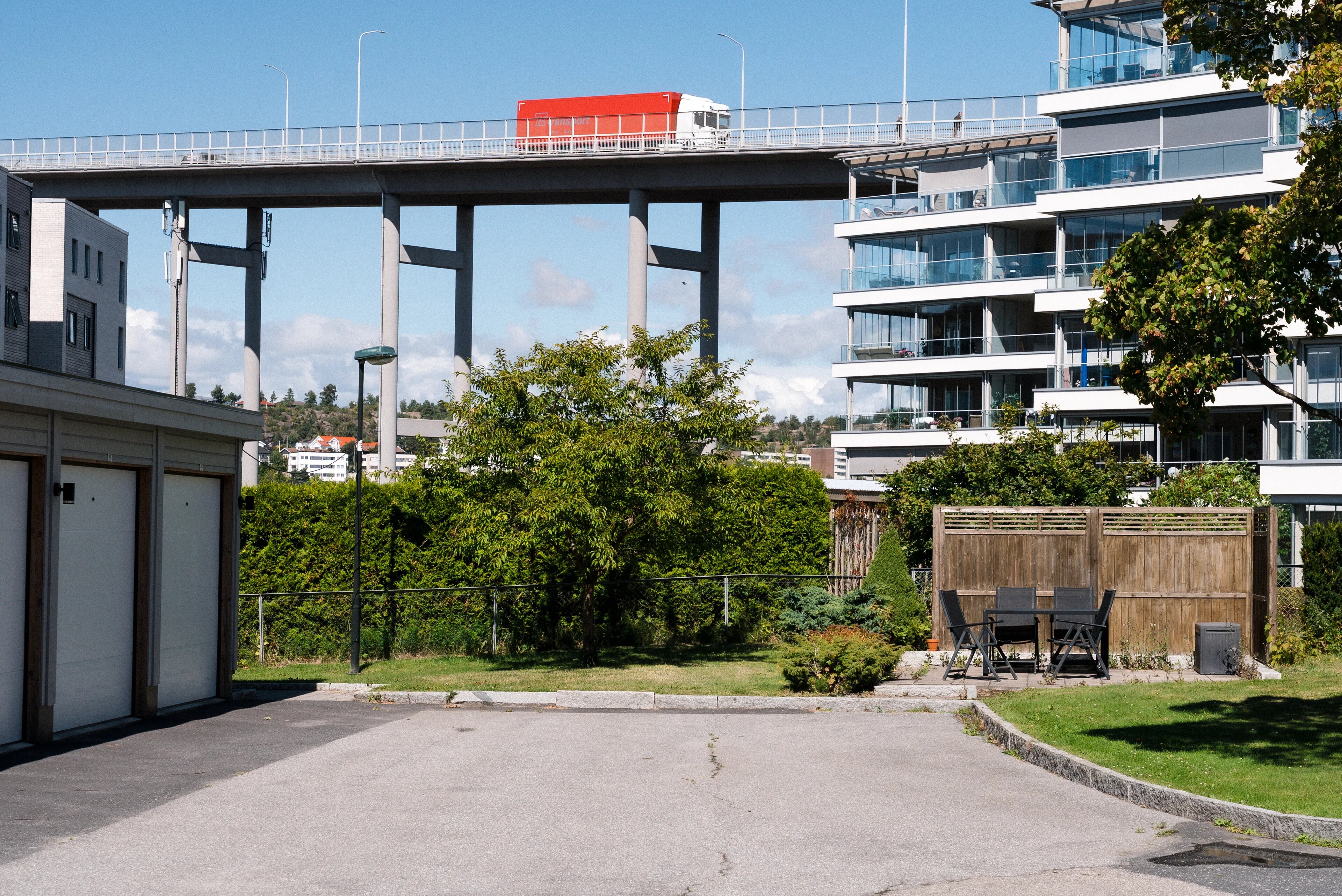 En rød lastebil kjører over en høy motorveibru ved en boligblokk. (Bildebeskrivelsen er laget av en KI-tjeneste)