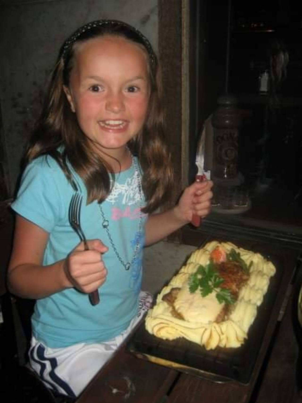 Andrine sitter på restaurant gliser til kamera og holder kniv og gaffel opp i lufta.