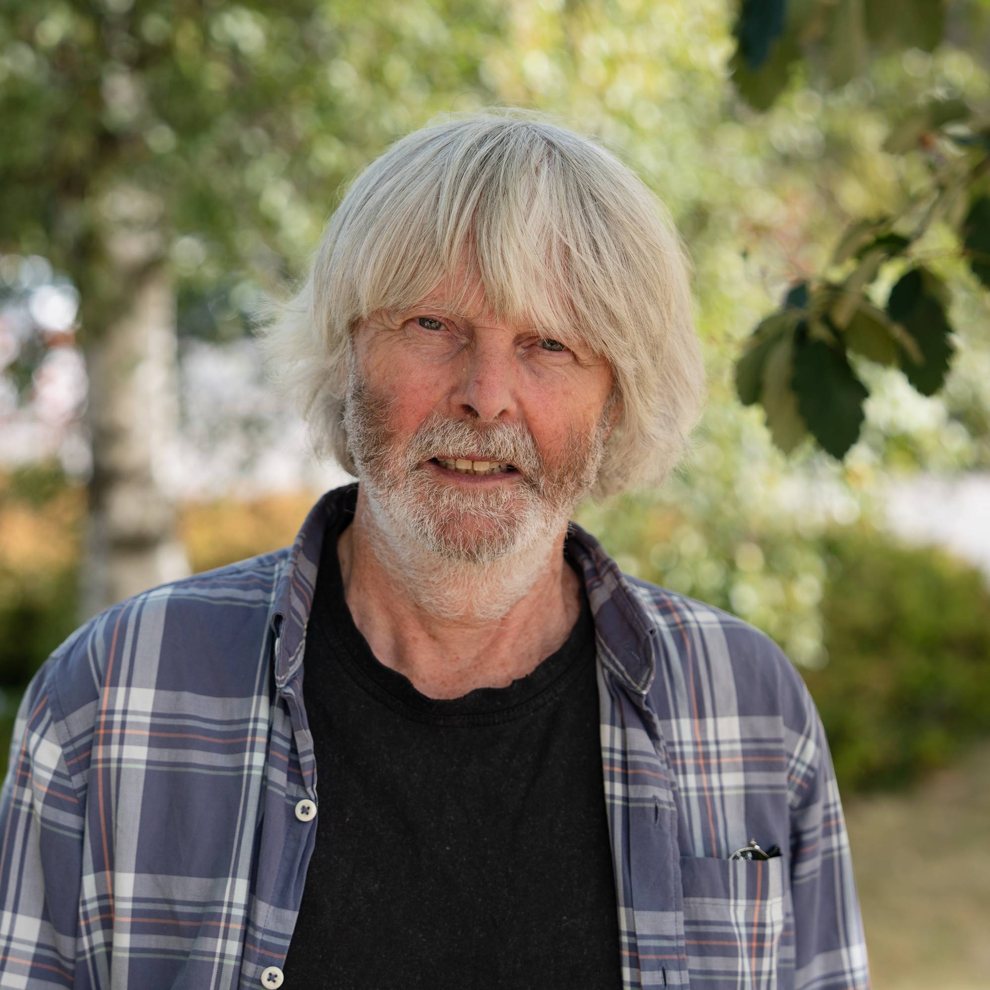 Portrett av en eldre mann med grått hår og skjegg, iført rutete skjorte, utendørs. (Bildebeskrivelsen er laget av en KI-tjeneste)