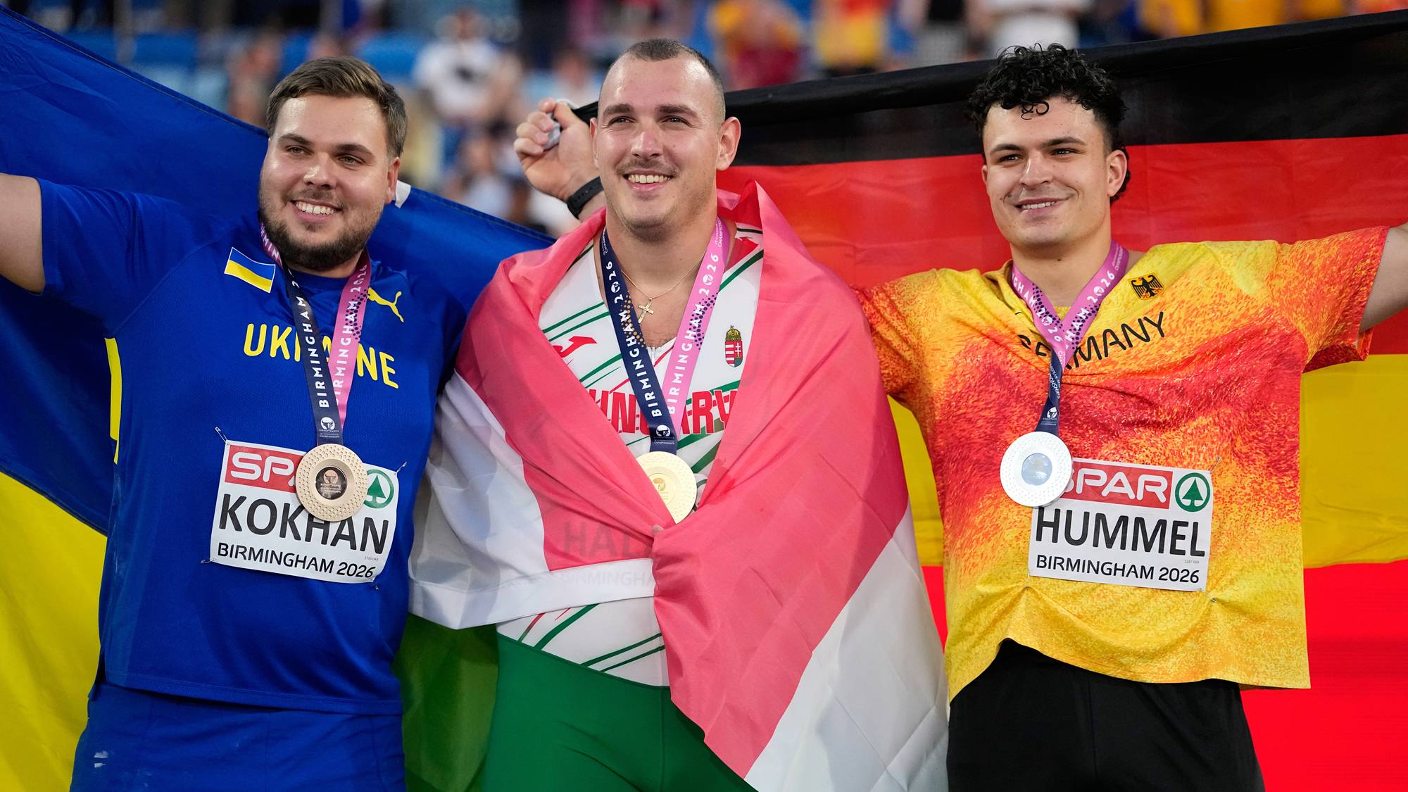 Medaljevinnere i friidrett med nasjonalflagg fra Ukraina, Ungarn og Tyskland etter en seremoni. (Bildebeskrivelsen er laget av en KI-tjeneste)