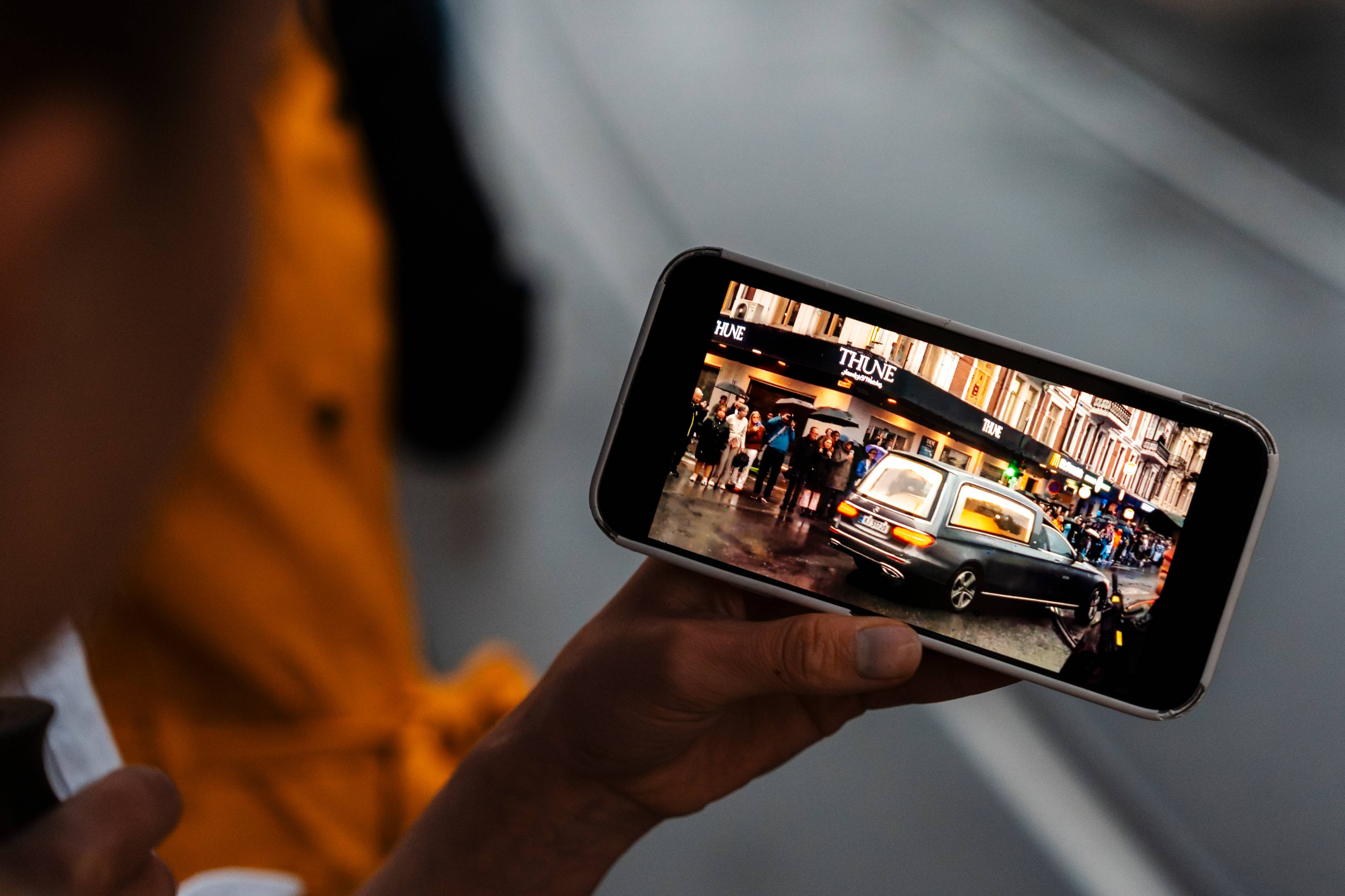 Person holder mobiltelefon som viser en bilkortesje i en bygate.