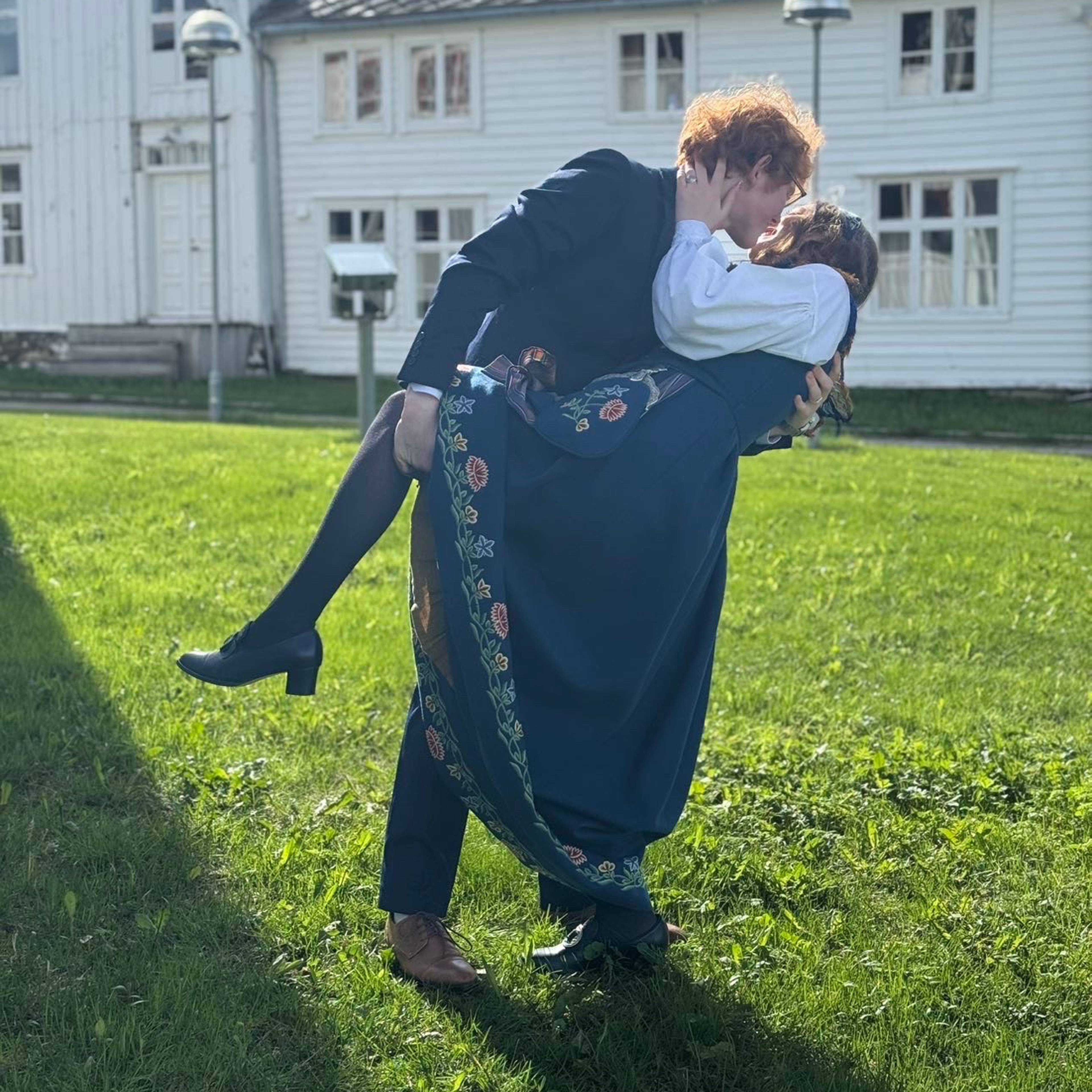 En ung mann i dress som kysser kjæresten sin som er kledd i bunad.
