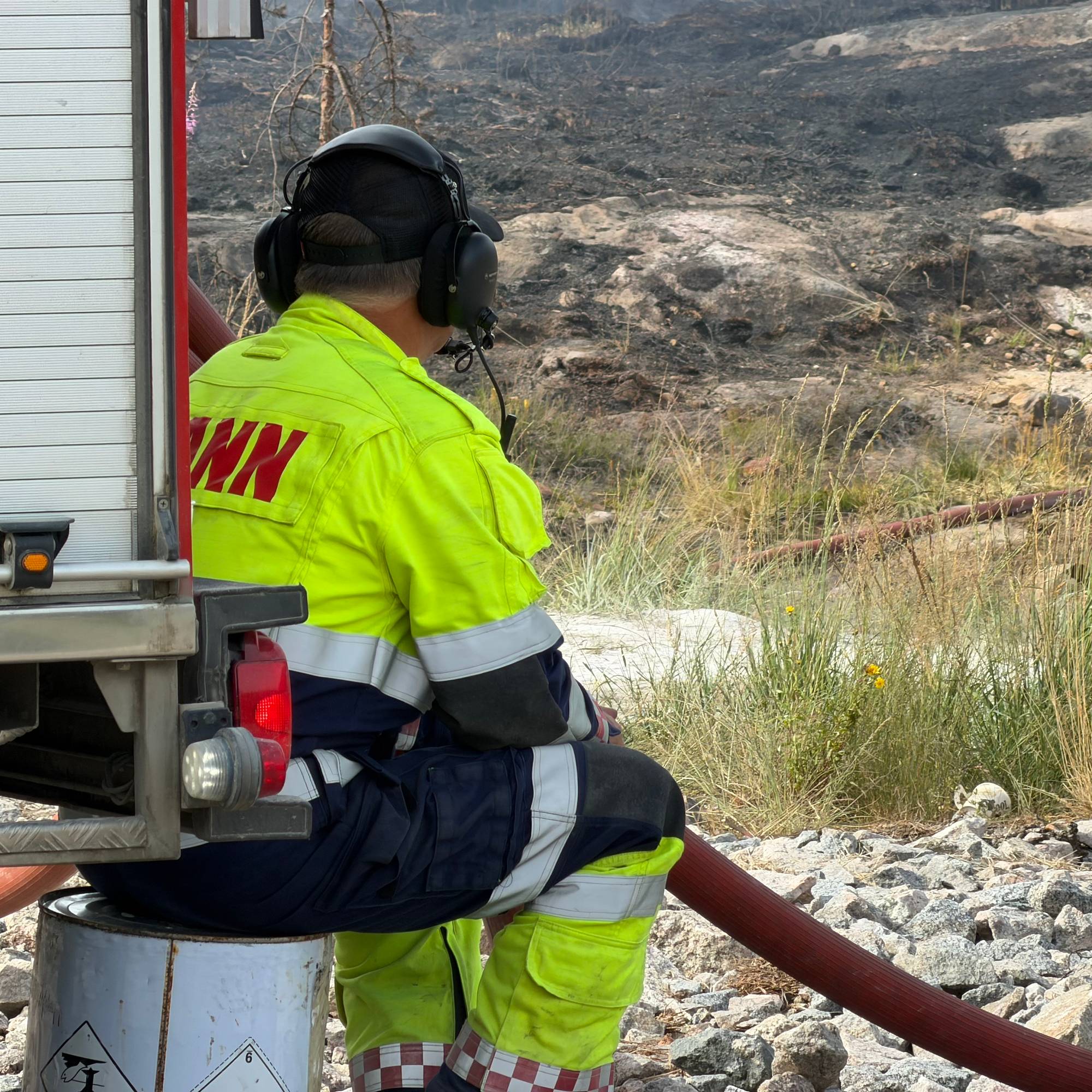 En brannmann sitter med en vannslange og ser på nedbrent landskap