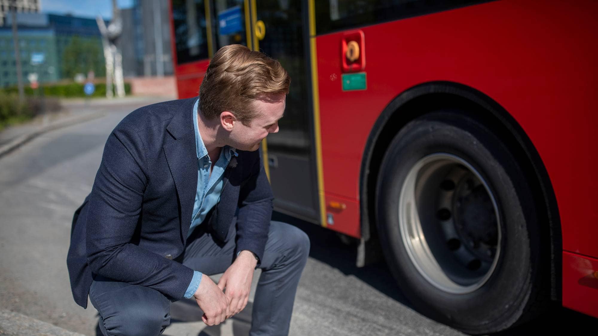 Mann i dressjakke ser på busshjul