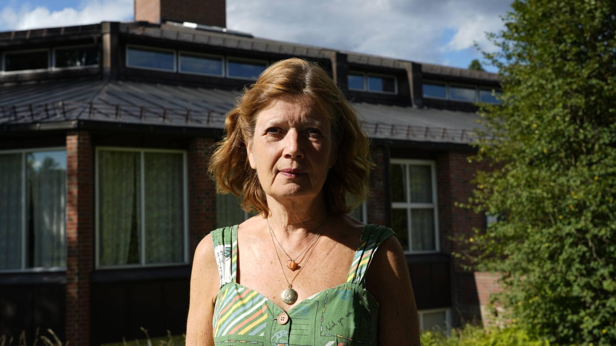 En kvinne med halvlangt hår og grønn kjole ser inn i kamera. 