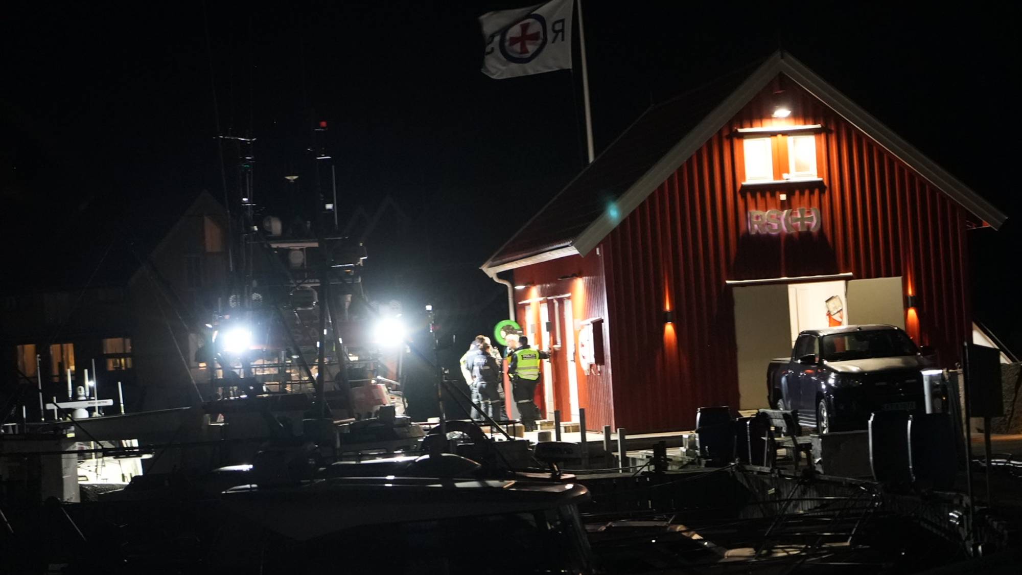 Nattbilde med opplyst redningsselskapshus og mannskaper.