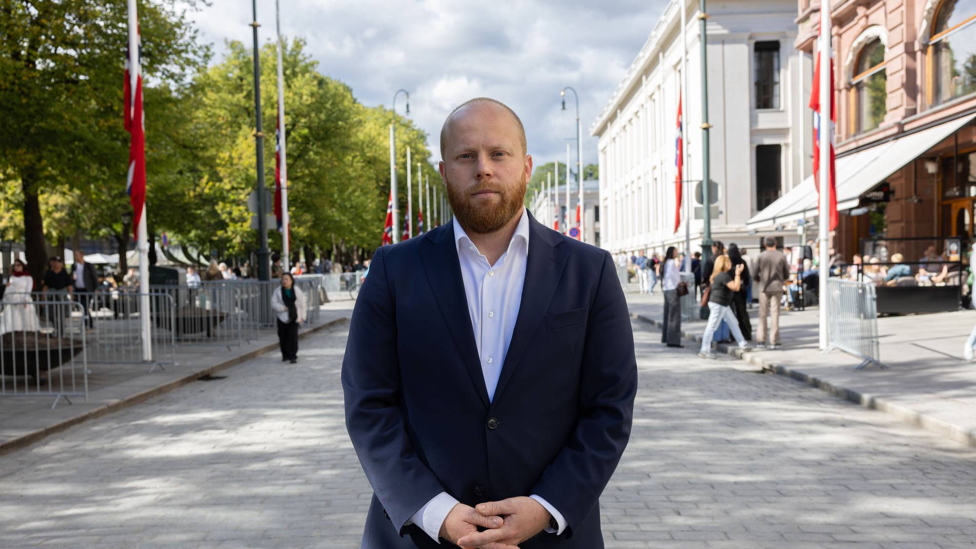 Men mann i mørk dress står i Karl Johan foran flagg på halv stang.