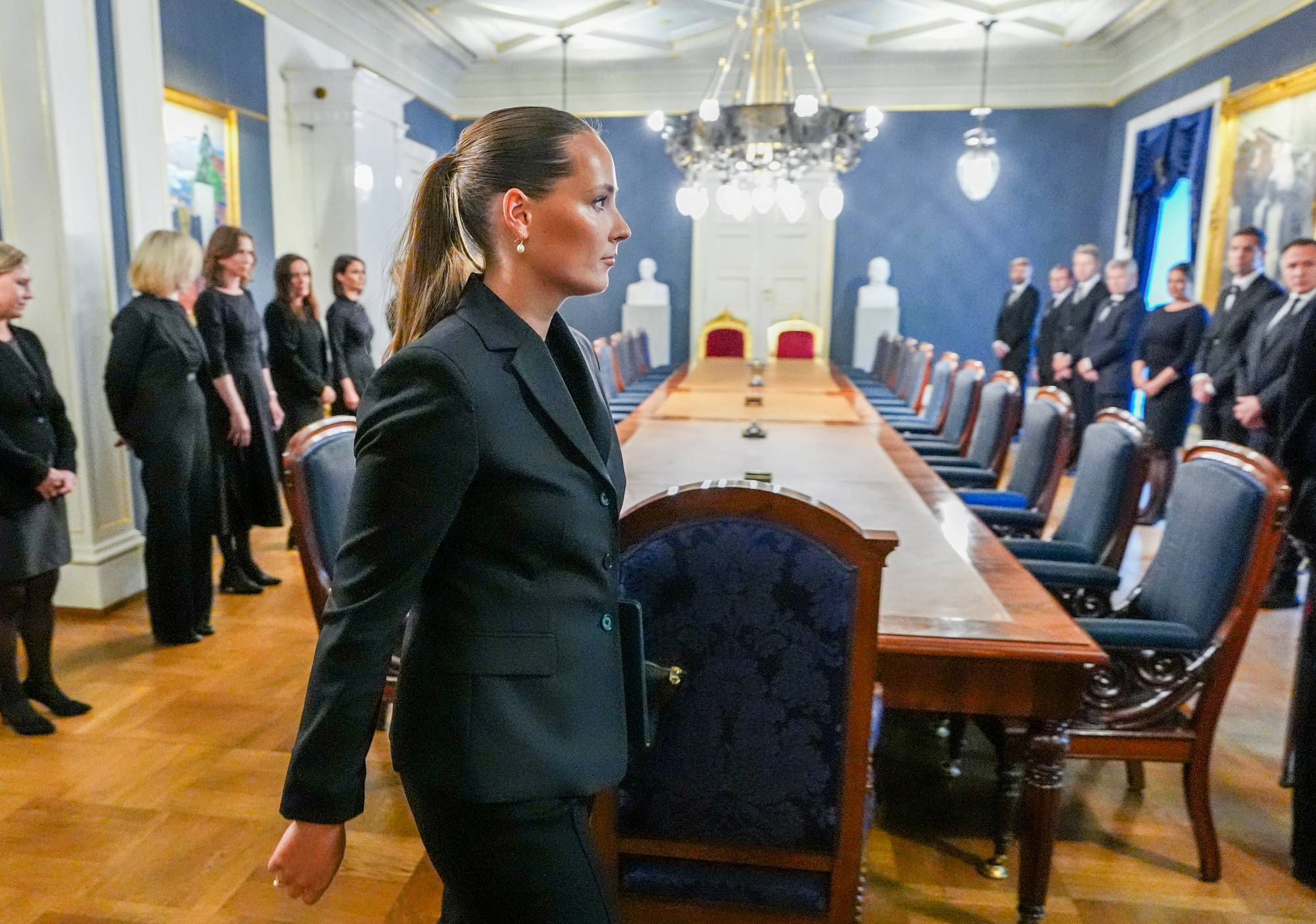 Kronprinsesse Ingrid Alexandra i dress går forbi et langt bord. Langs bordet står regjeringsmedlemmer i dress.