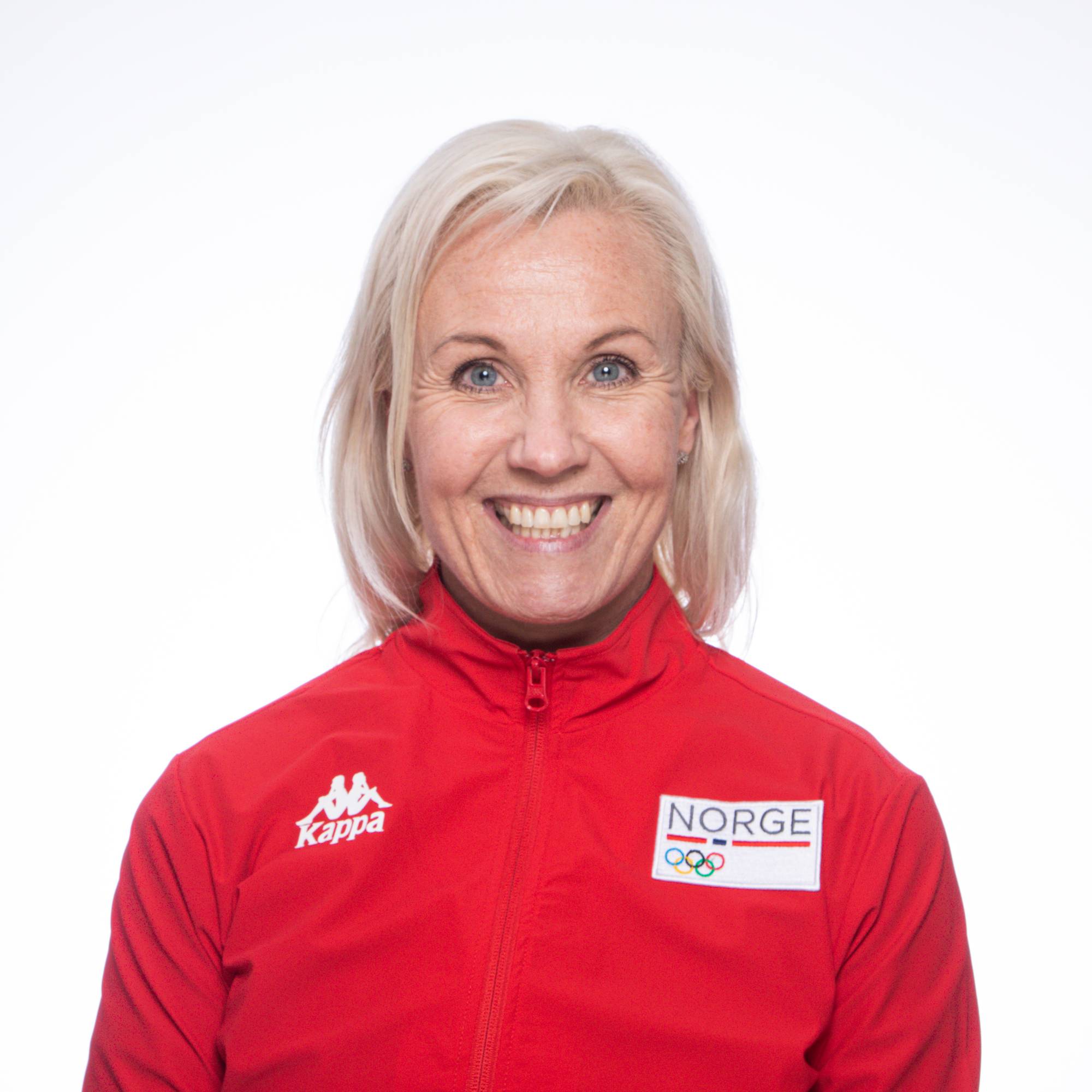 Personen står med en nøytral bakgrunn iført en rød jakke med teksten "Norge" og olympiske ringer. Det er en utydelig ansiktspresentasjon. Personen har lengre, lyst hår. (Bildebeskrivelsen er laget av en KI-tjeneste)