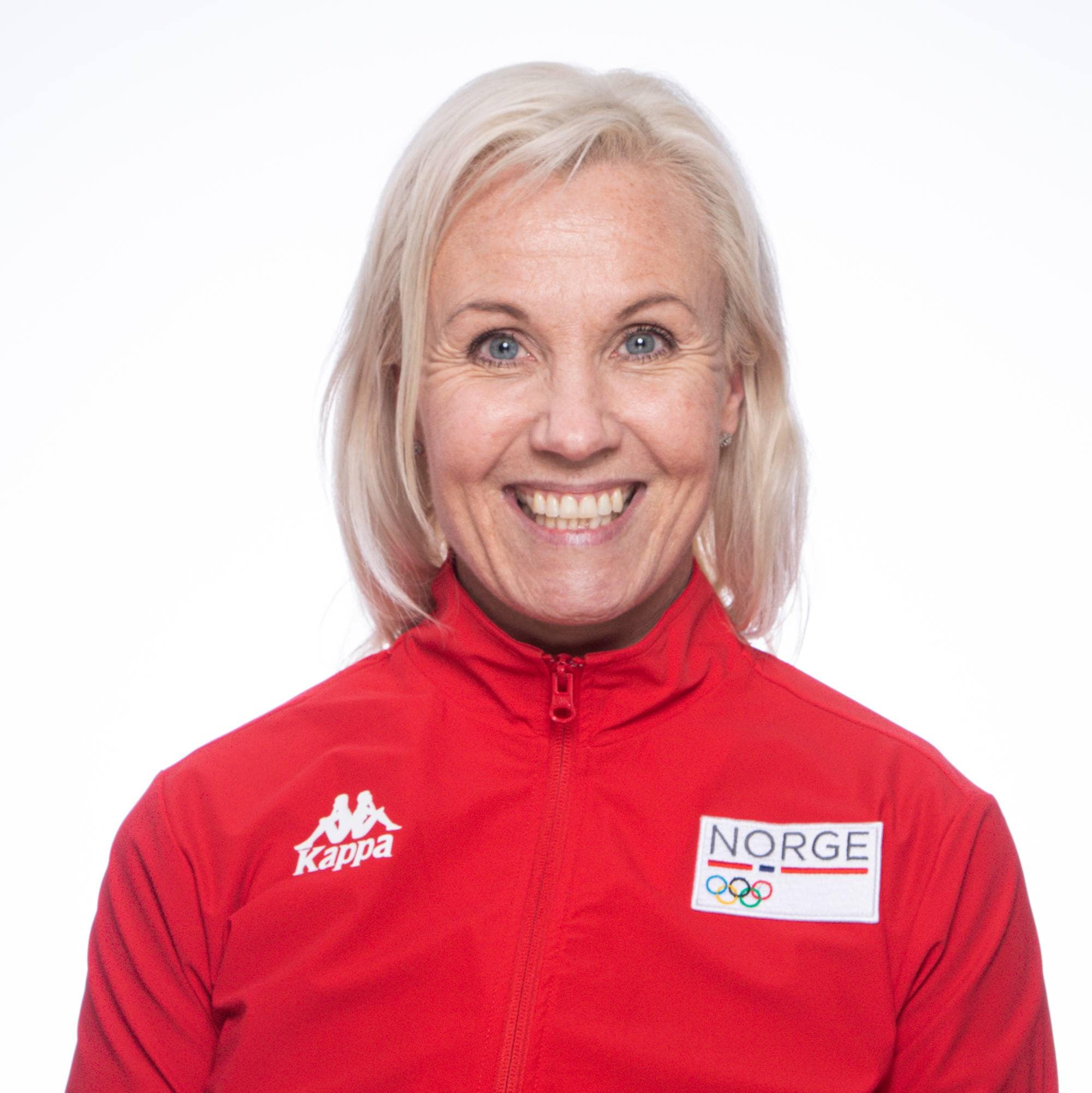 Personen står med en nøytral bakgrunn iført en rød jakke med teksten "Norge" og olympiske ringer. Det er en utydelig ansiktspresentasjon. Personen har lengre, lyst hår. (Bildebeskrivelsen er laget av en KI-tjeneste)