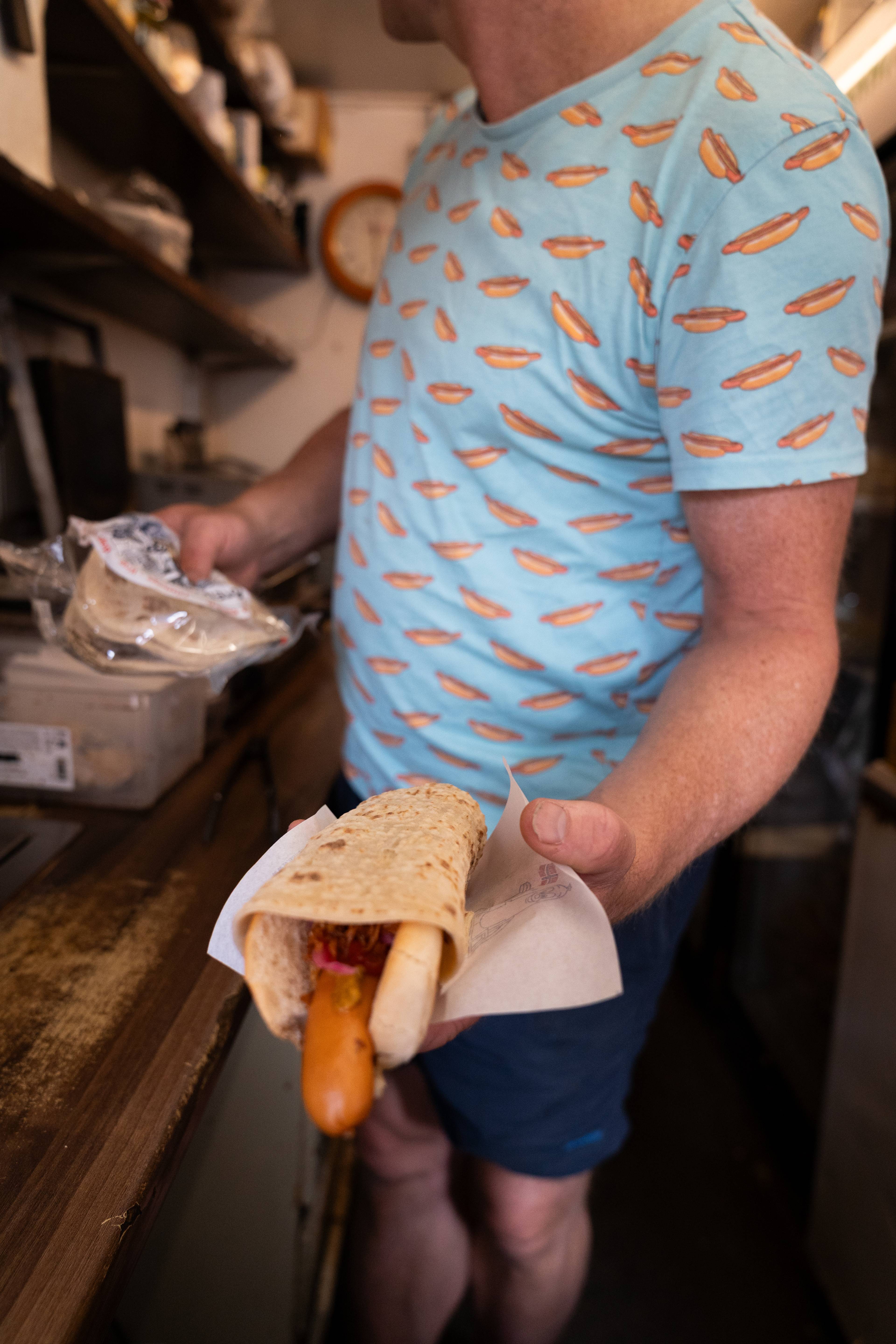 en person som holder en pølse med lompe på toppen