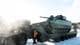 Torbjørn Kjosvold / Forsvaret / Forsvaret Et militært kjøretøy, en stridsvogn, står lastet på en transporttrailer i snølagt terreng. Sollyset skaper refleksjoner og glimt gjennom bildet, som viser klar himmel. Kjøretøyet har en militærgrønn farge og tydelige identifikasjonsnumre. Ingen personer er synlige i bildet. (Bildebeskrivelsen er laget av en KI-tjeneste)